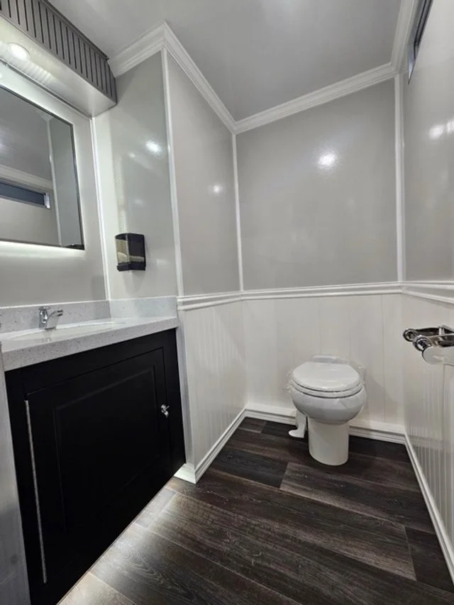 Small bathroom with a white toilet, black vanity with white countertop, and a mirror with built-in lighting.