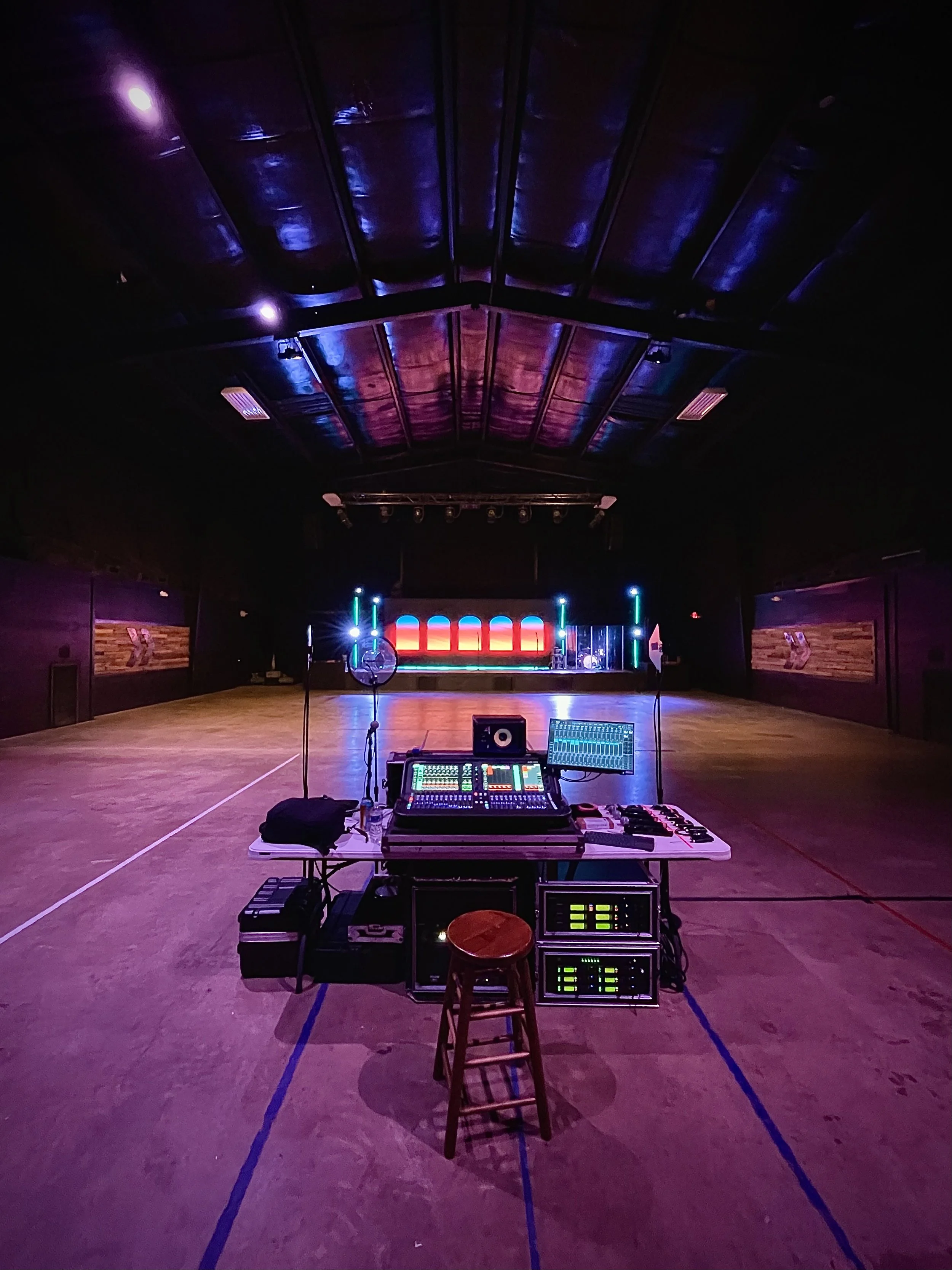Empty dance floor with colorful stage lighting, sound equipment, and a stool in the foreground.
