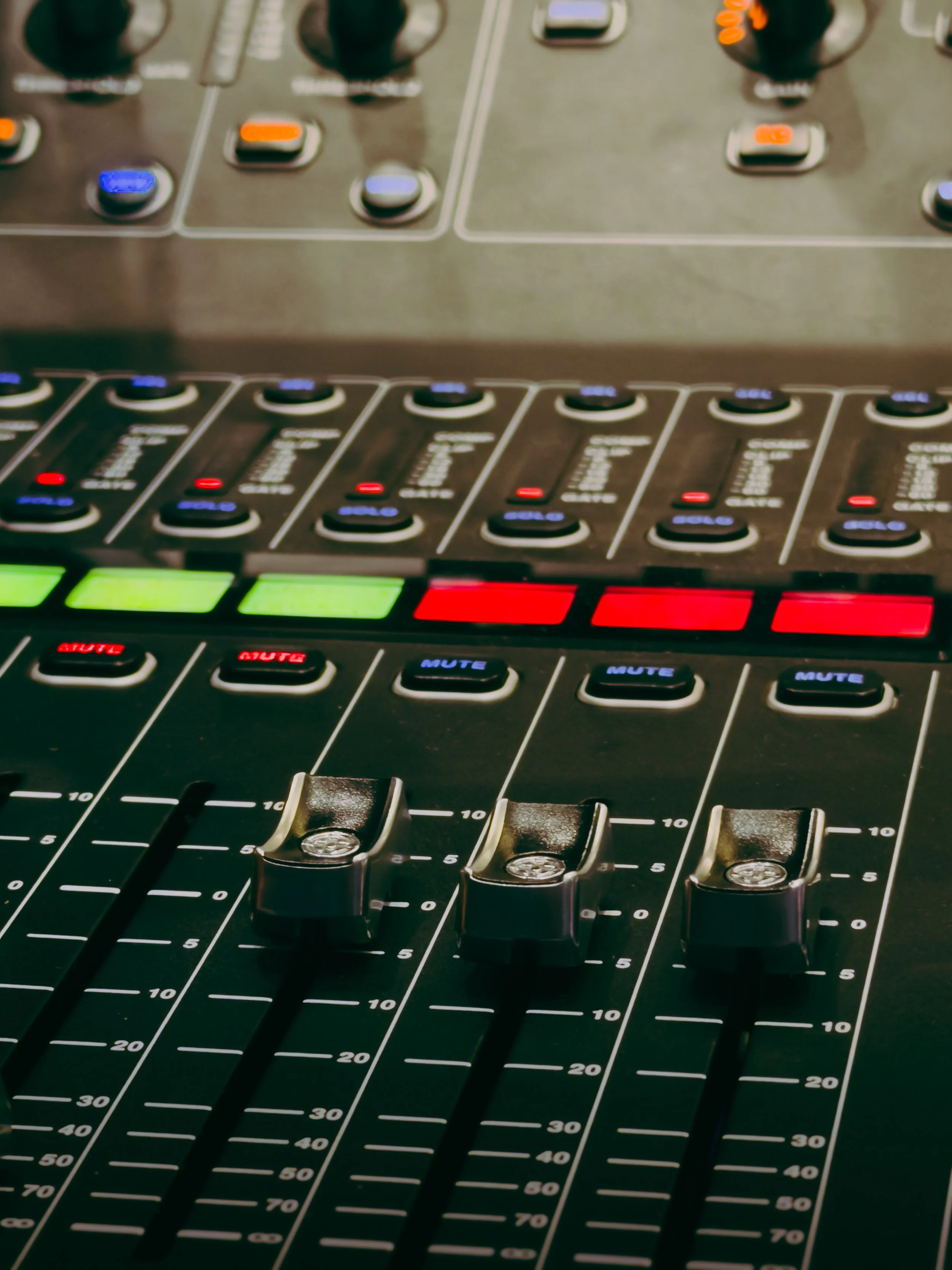 Close-up of a professional audio mixing console showing sliders, buttons, and color-coded indicators.