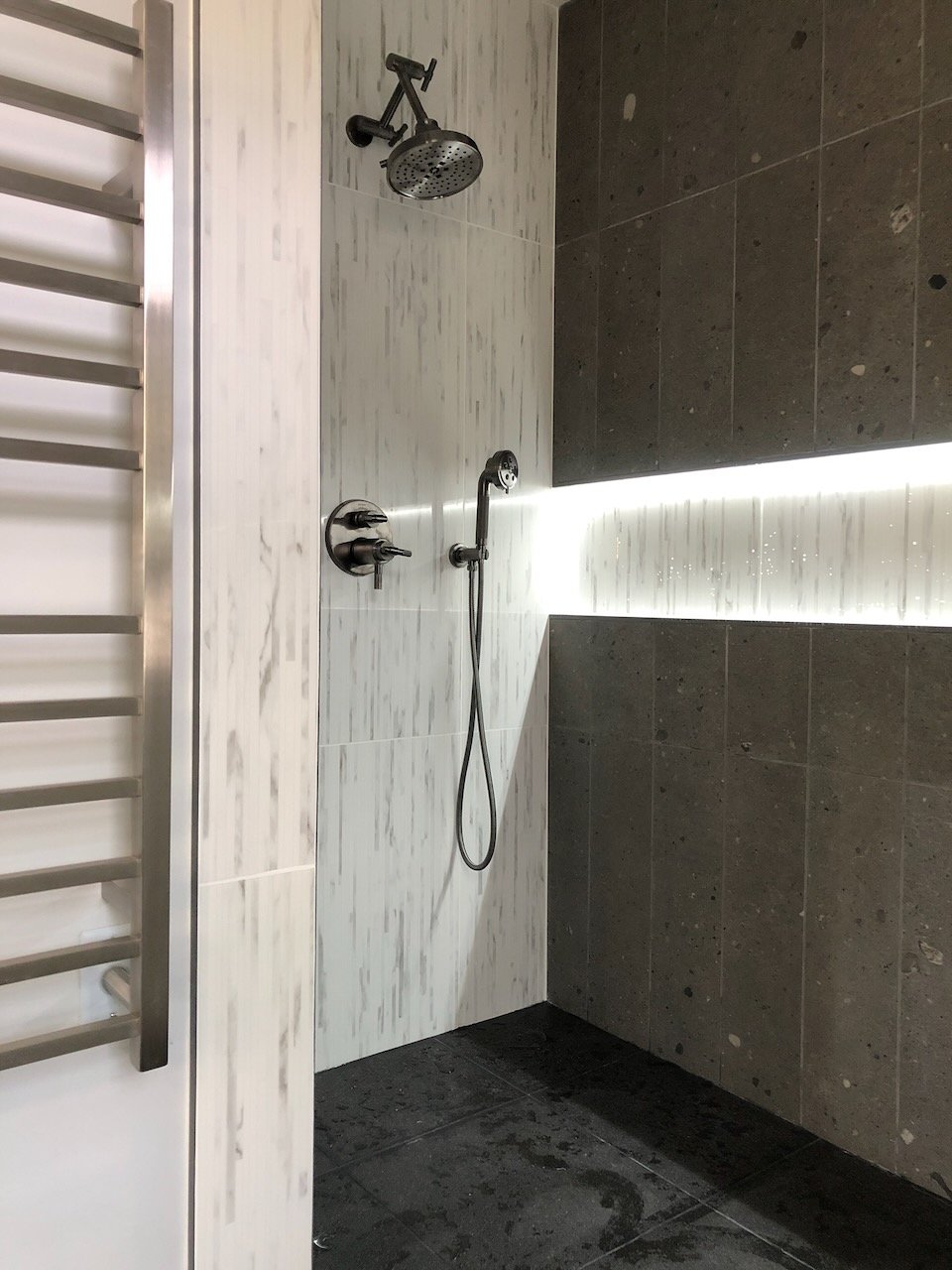 Custom tiled shower with a long recessed niche and handheld shower.
