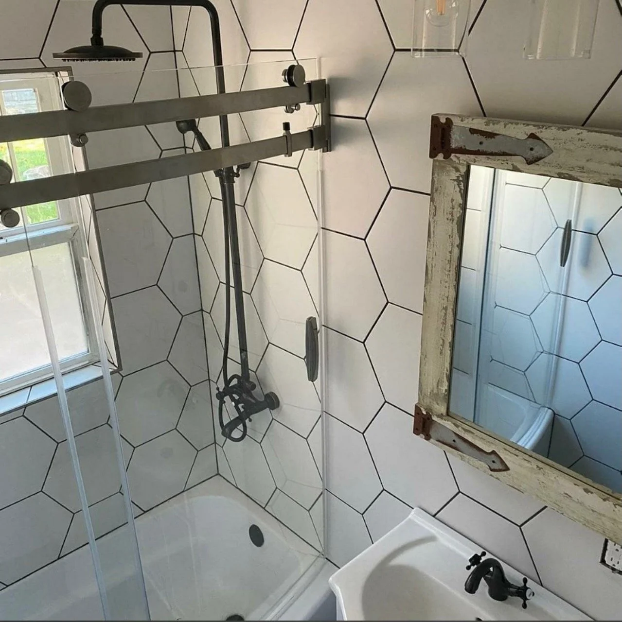 White bathroom with geometric wall tile, glass shower doors and black fixtures.