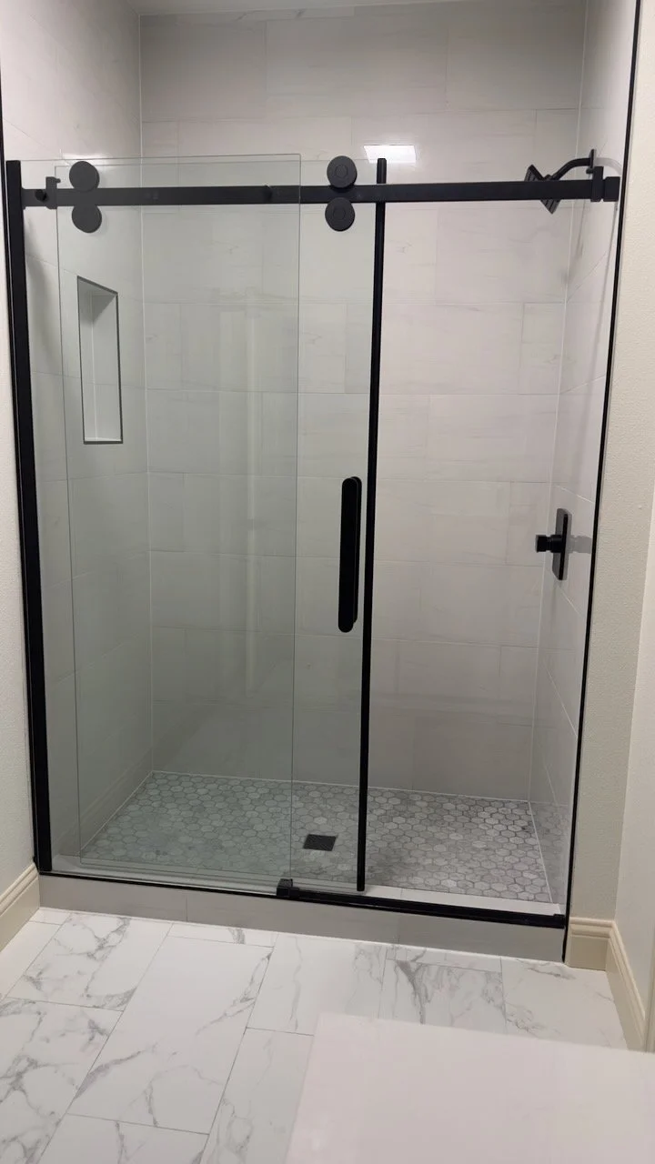 Glass shower enclosure with black sliding-door hardware and light tile.