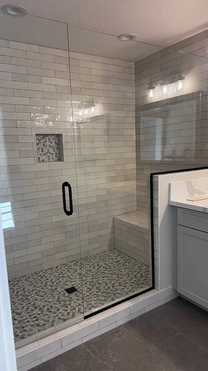 Glass-enclosed shower with gray tile and a mosaic shower floor.