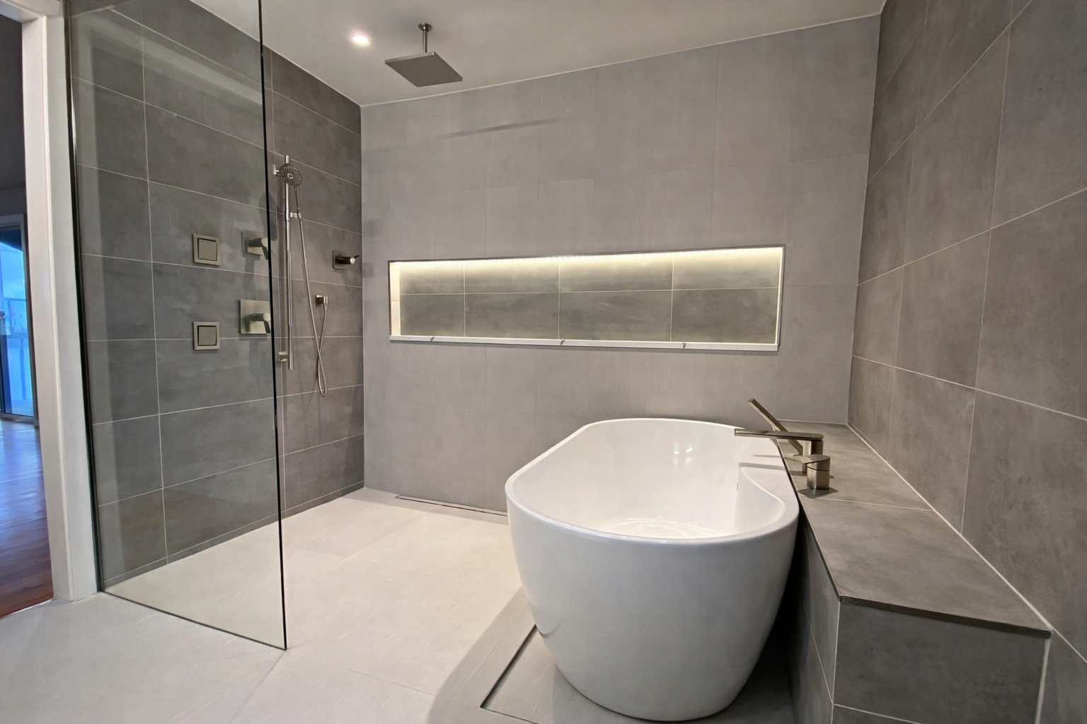 Modern bathroom with a freestanding bathtub, a walk-in shower with a glass door, gray tiled walls, and a sleek mirror with built-in lighting.