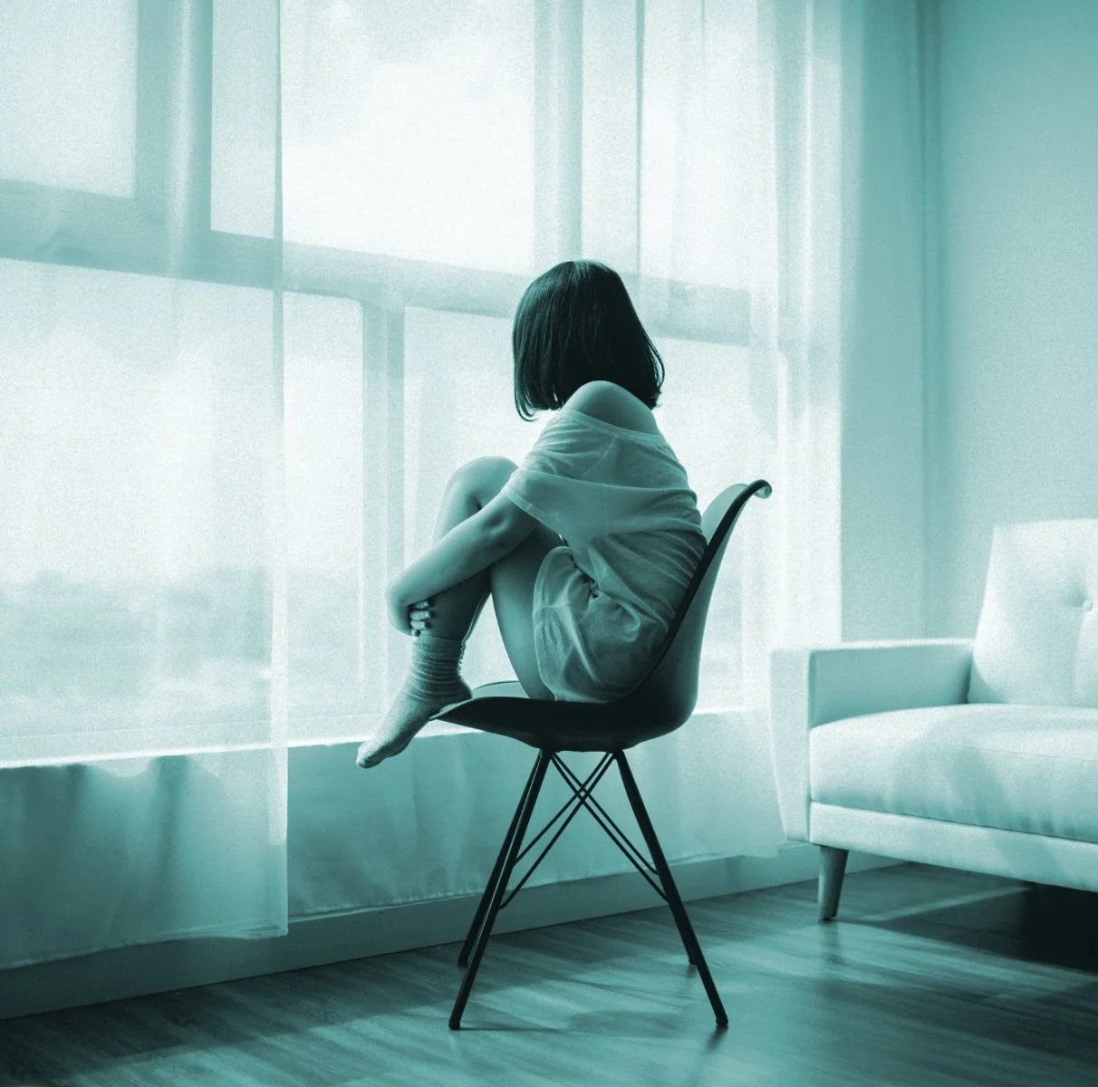 Woman sitting on a chair looking out of a window, representing reflection and healing through Kerry Christie’s self-help guides