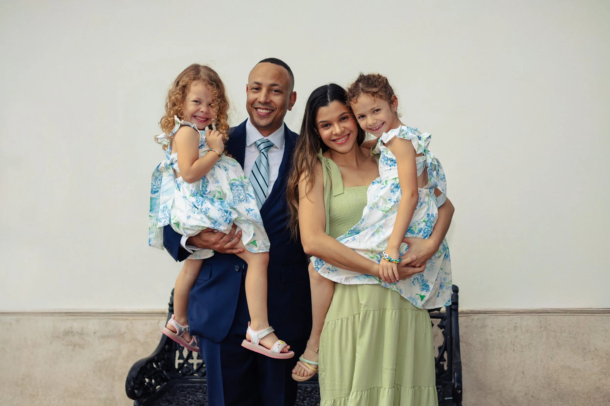 Harris family posing together, with he and his wife holding their two daughters, respectively, against a plain wall background.
