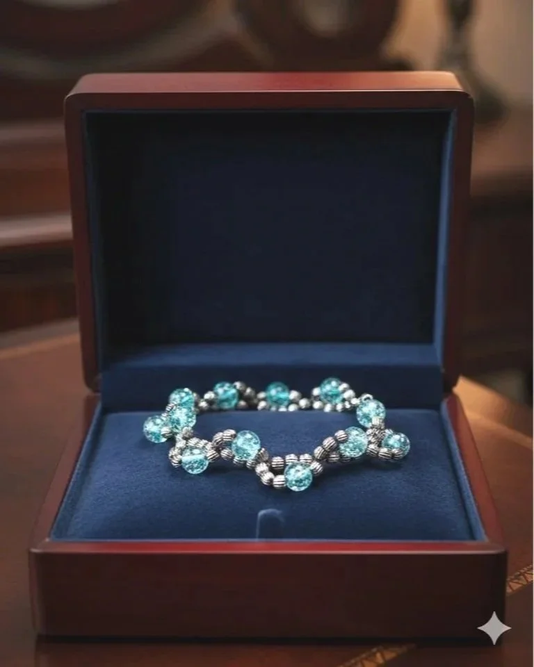 A bracelet with blue gemstones and silver beads displayed in an open wooden jewelry box with a dark blue interior.