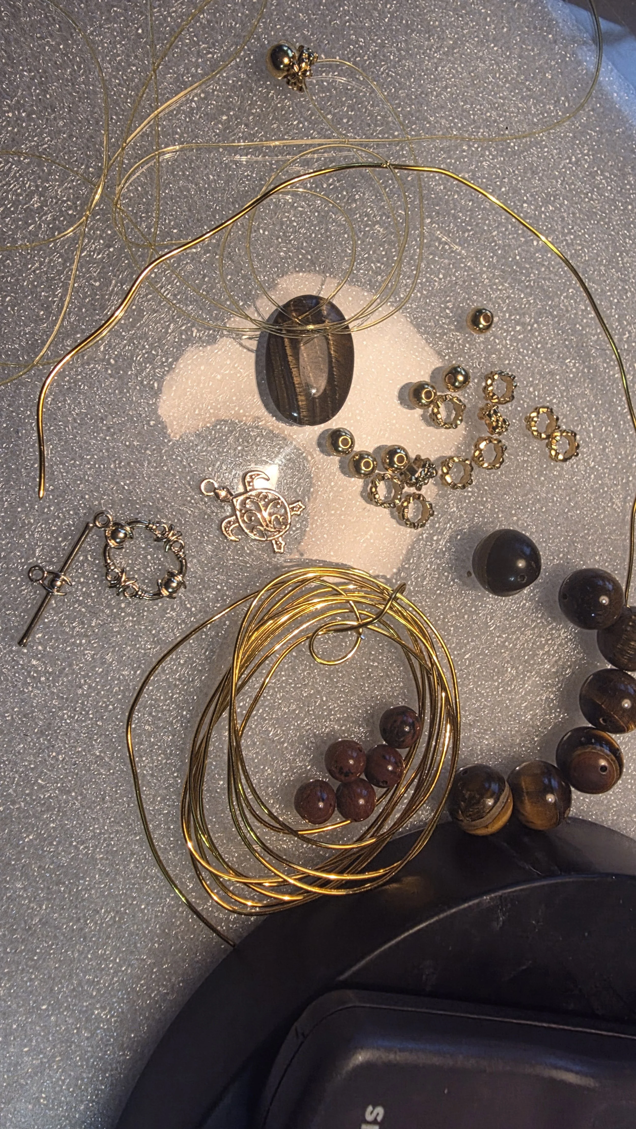 Various jewelry pieces including black beads, gold wire necklaces, and decorative charms are scattered on a textured gray surface.