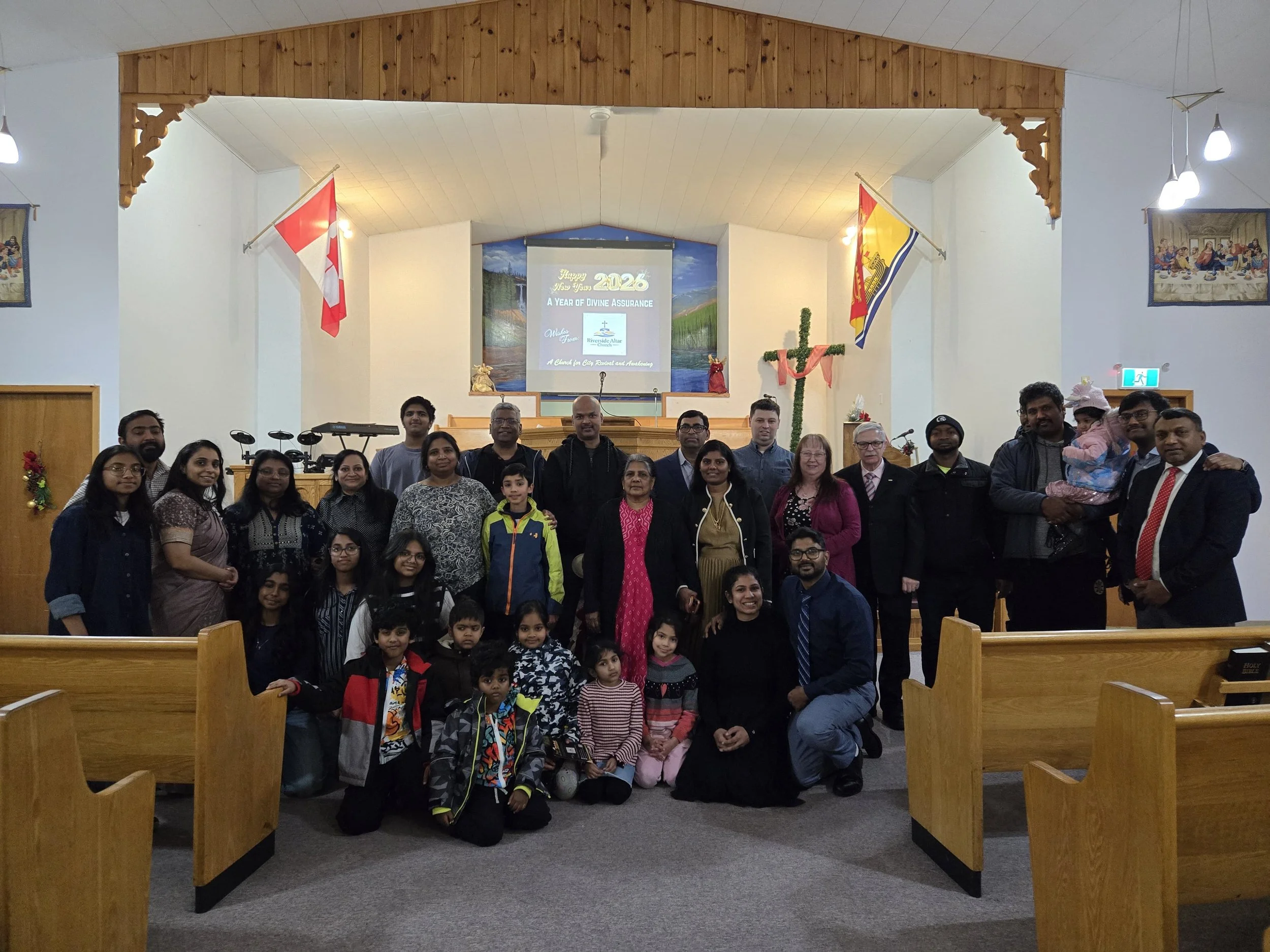 Group of people including children and adults posing together in a church, with combat, flags, and a cross in the background, celebrating New Year's 2024.
