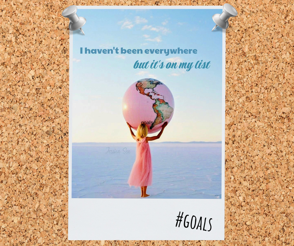 A girl in a pink dress holding a globe with the Americas, standing on a salt flat against a blue sky. Text on the image reads, "I haven't been everywhere but it's on my list," with the hashtag "#GOALS" at the bottom.