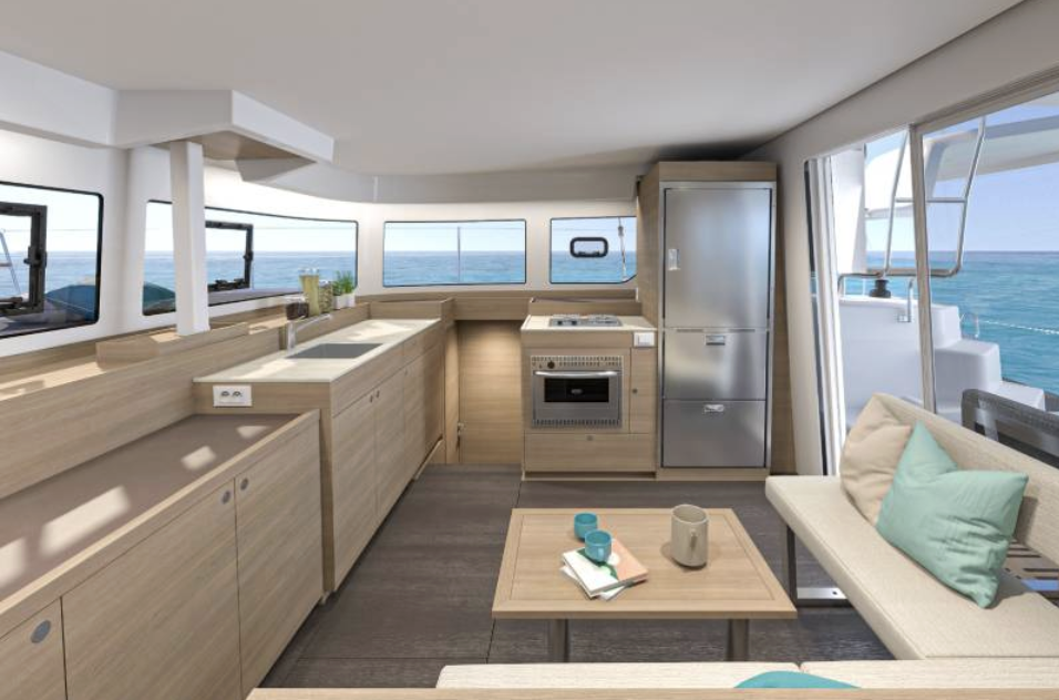 Interior of a boat or yacht with a compact kitchen, sofa with pillows, and large windows showing ocean view.