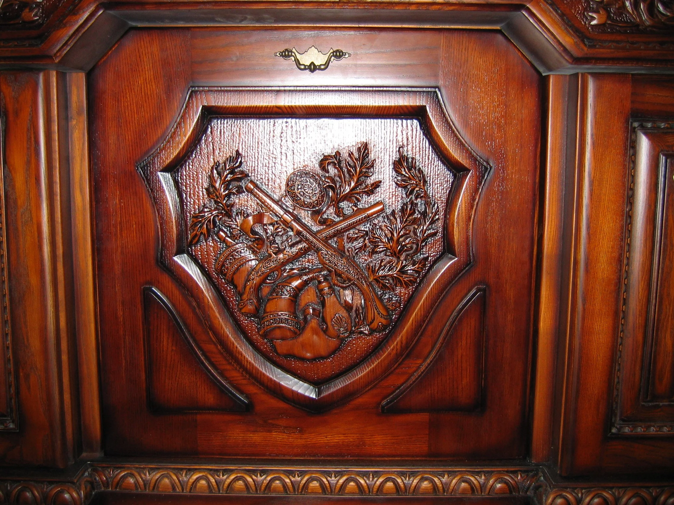 Intricate wooden carving of crossed muskets and foliage on a polished wooden surface.