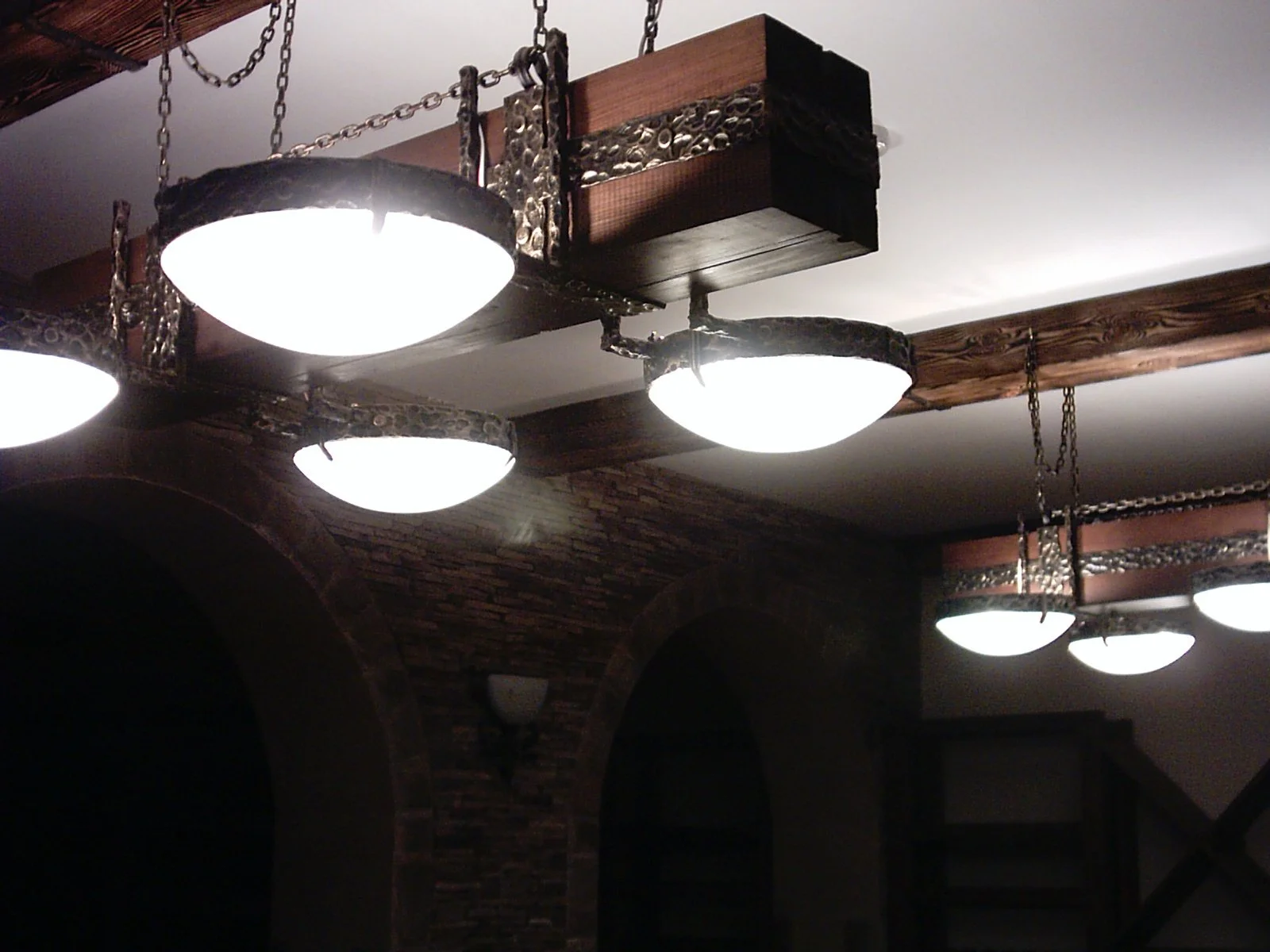 Ceiling lights with rustic wood and metal chains in a room with brick archways.