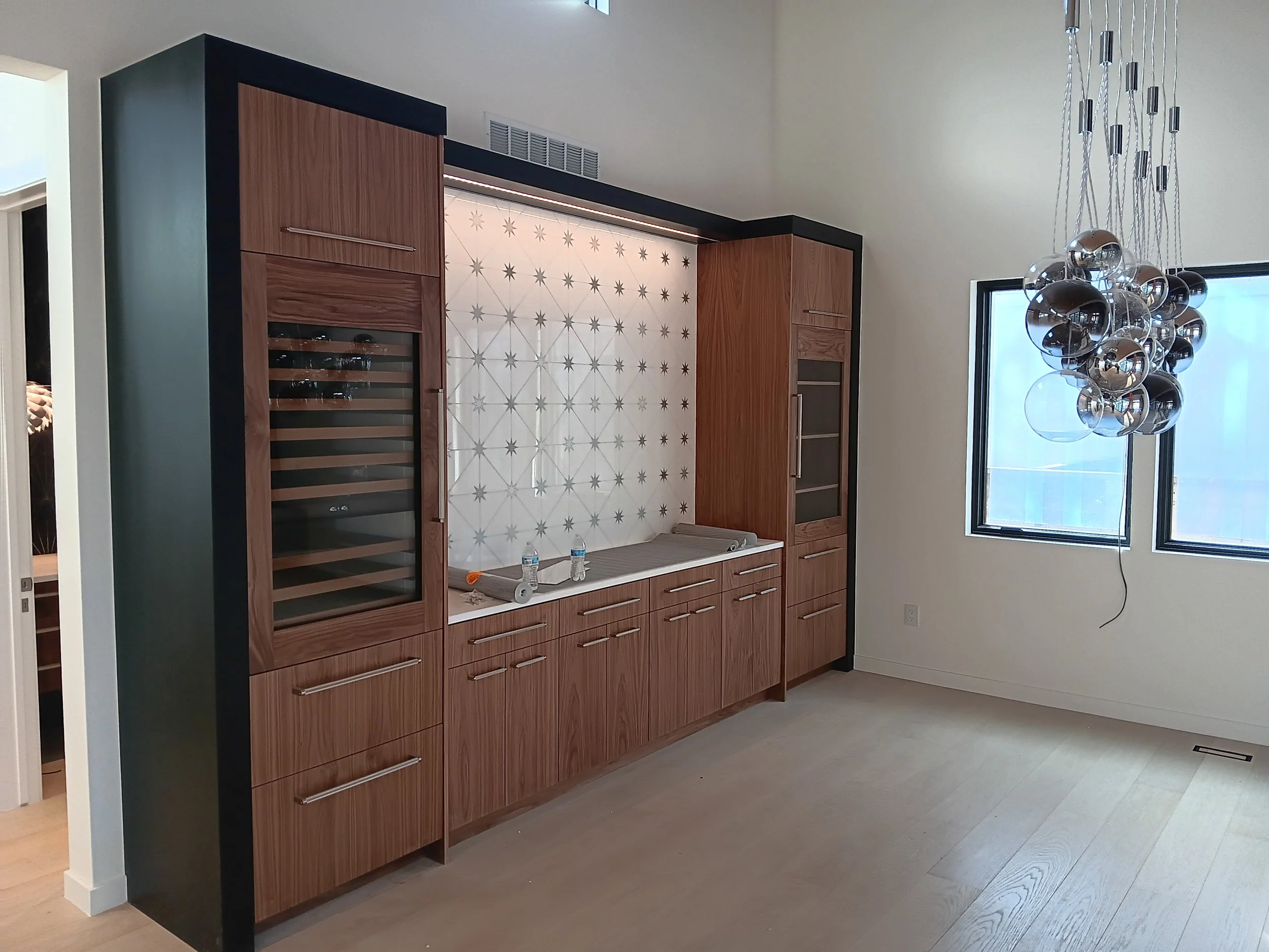 Kitchen with wooden cabinets, a wine cooler, decorative backsplash, and a cluster of modern metallic pendant lights near windows.