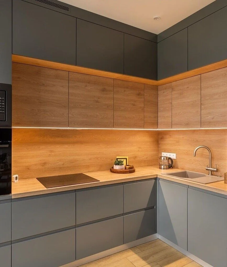 Modern kitchen with gray lower cabinets, wood upper cabinets, and a wood backsplash. Includes a black cooktop, a small plant on a tray, a stainless steel kettle, and a sink with a curved faucet.