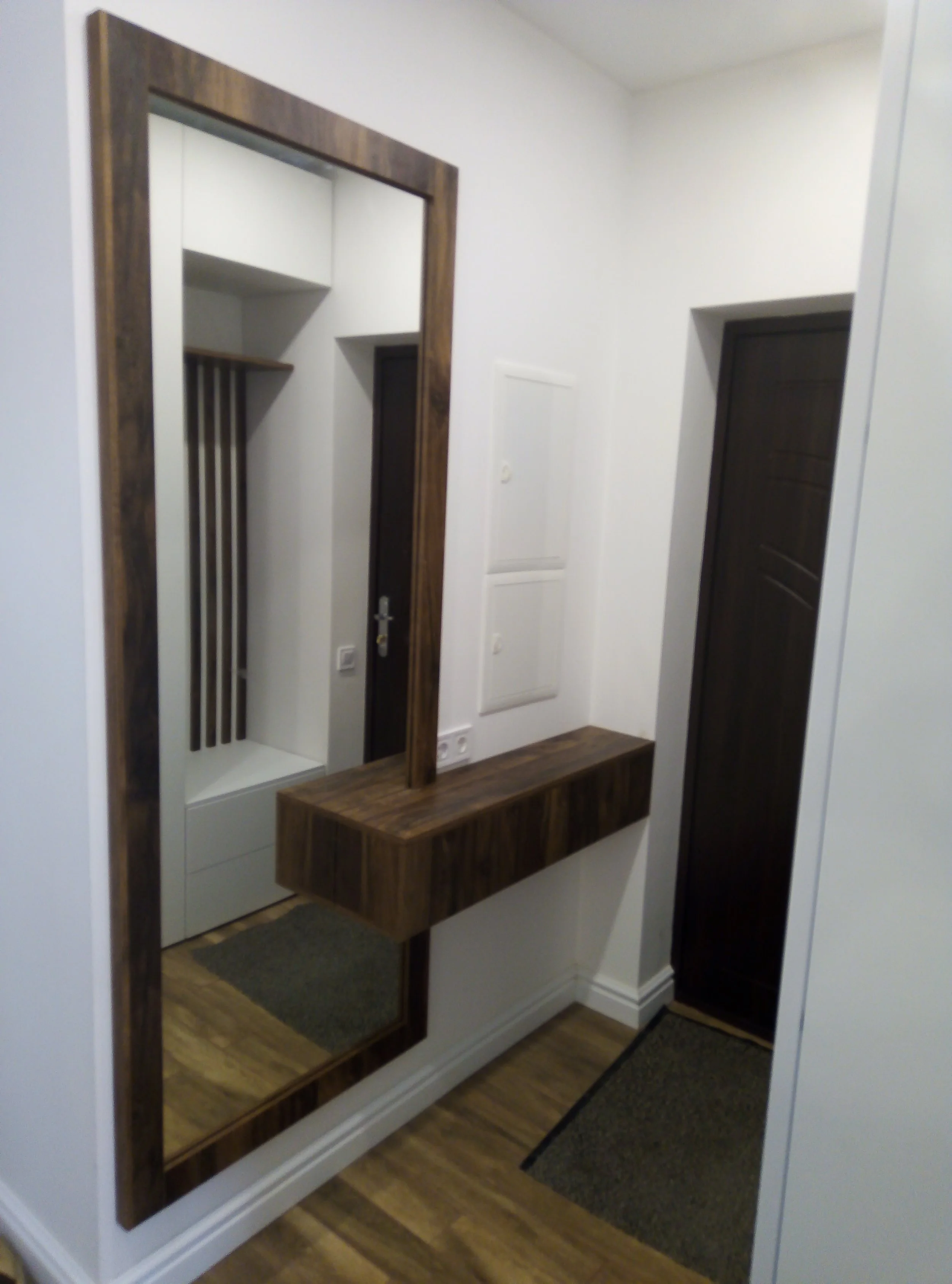 Entryway with a large wall mirror, a wooden console table, and a coat rack with vertical wooden slats.
