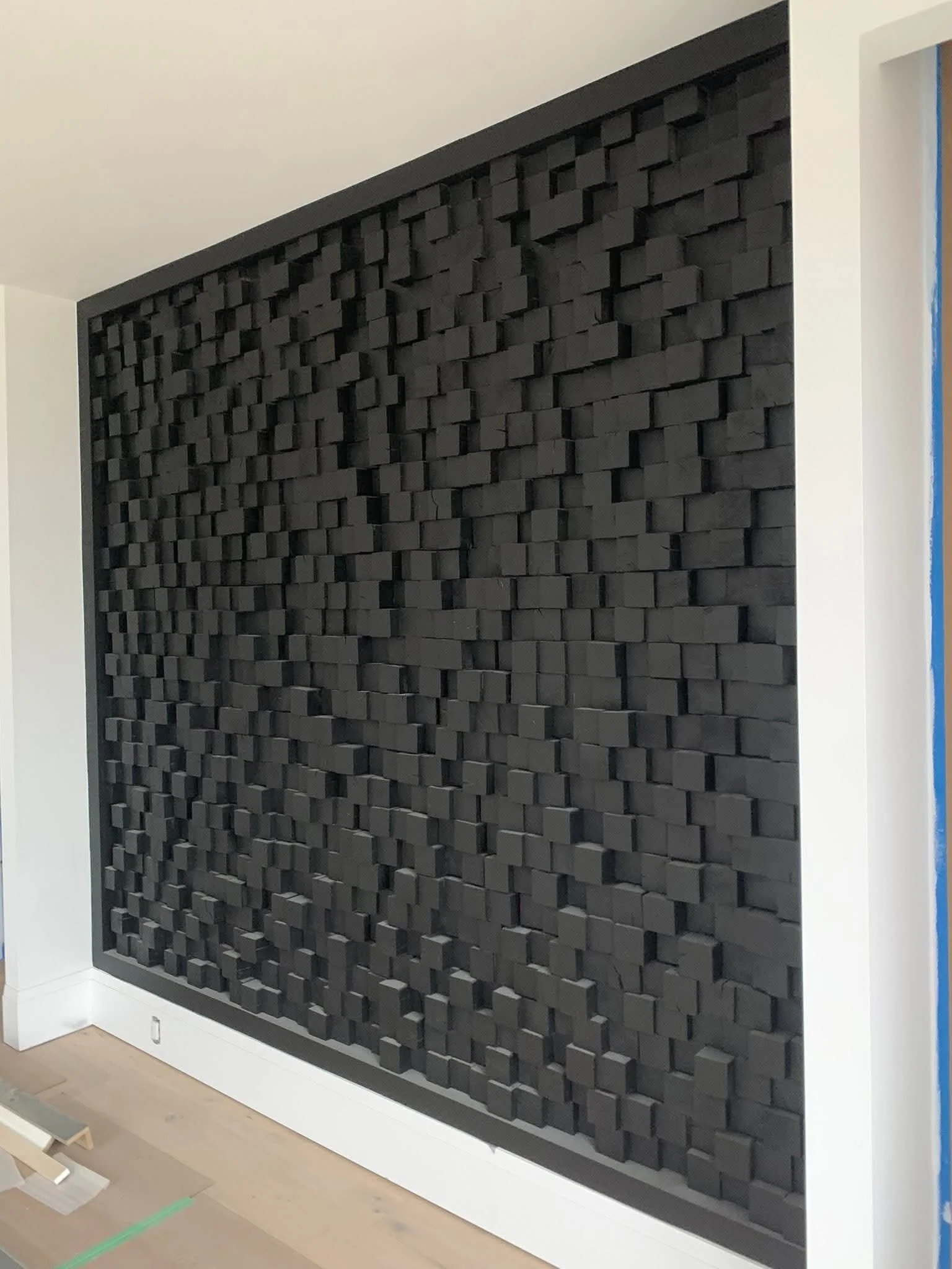 A black acoustic wall panel with a three-dimensional brick pattern in a room with white trim and light wood flooring.