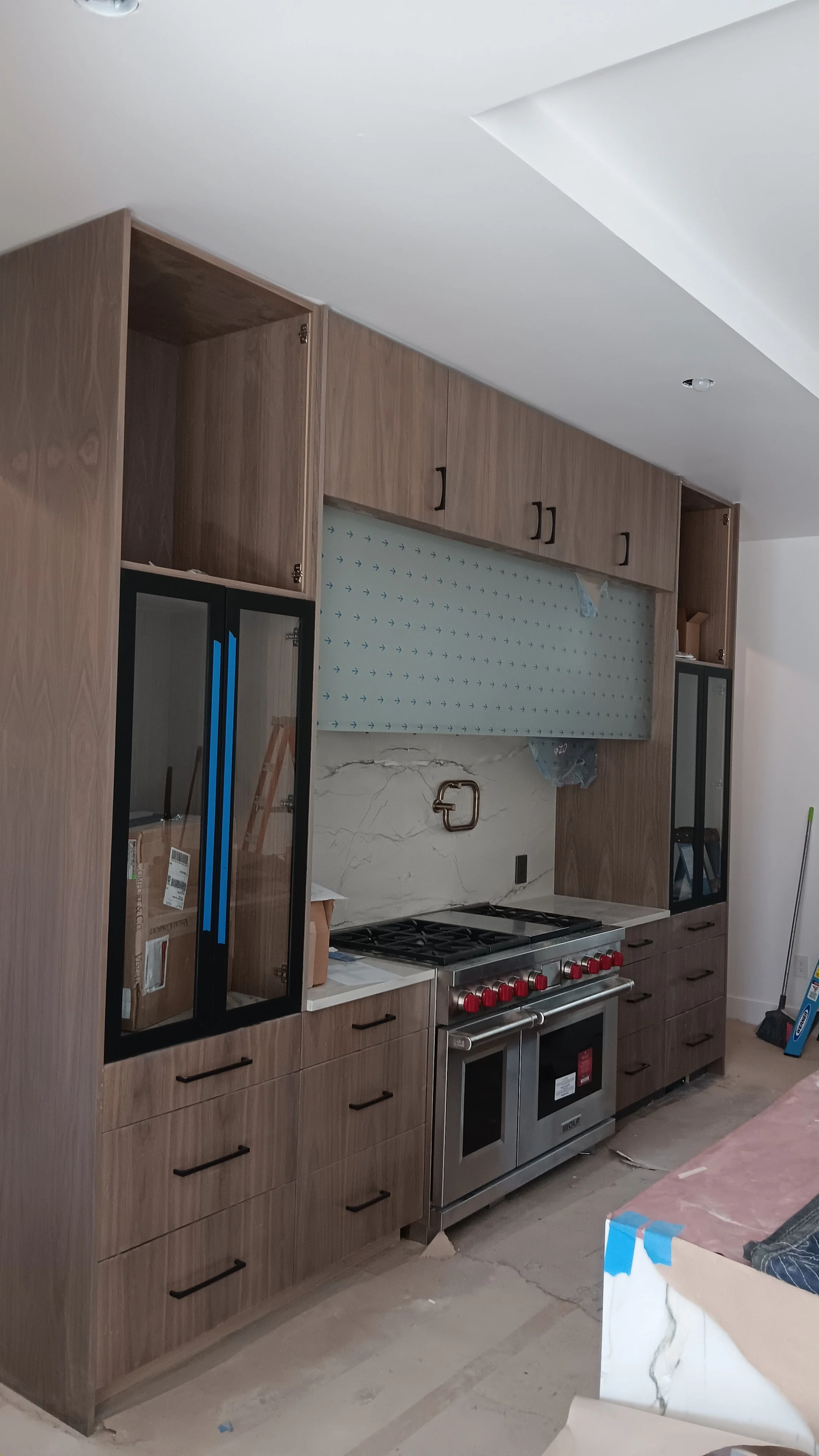 Kitchen under construction with wooden cabinets, a stainless steel stove, and a marble backsplash, with construction materials nearby.