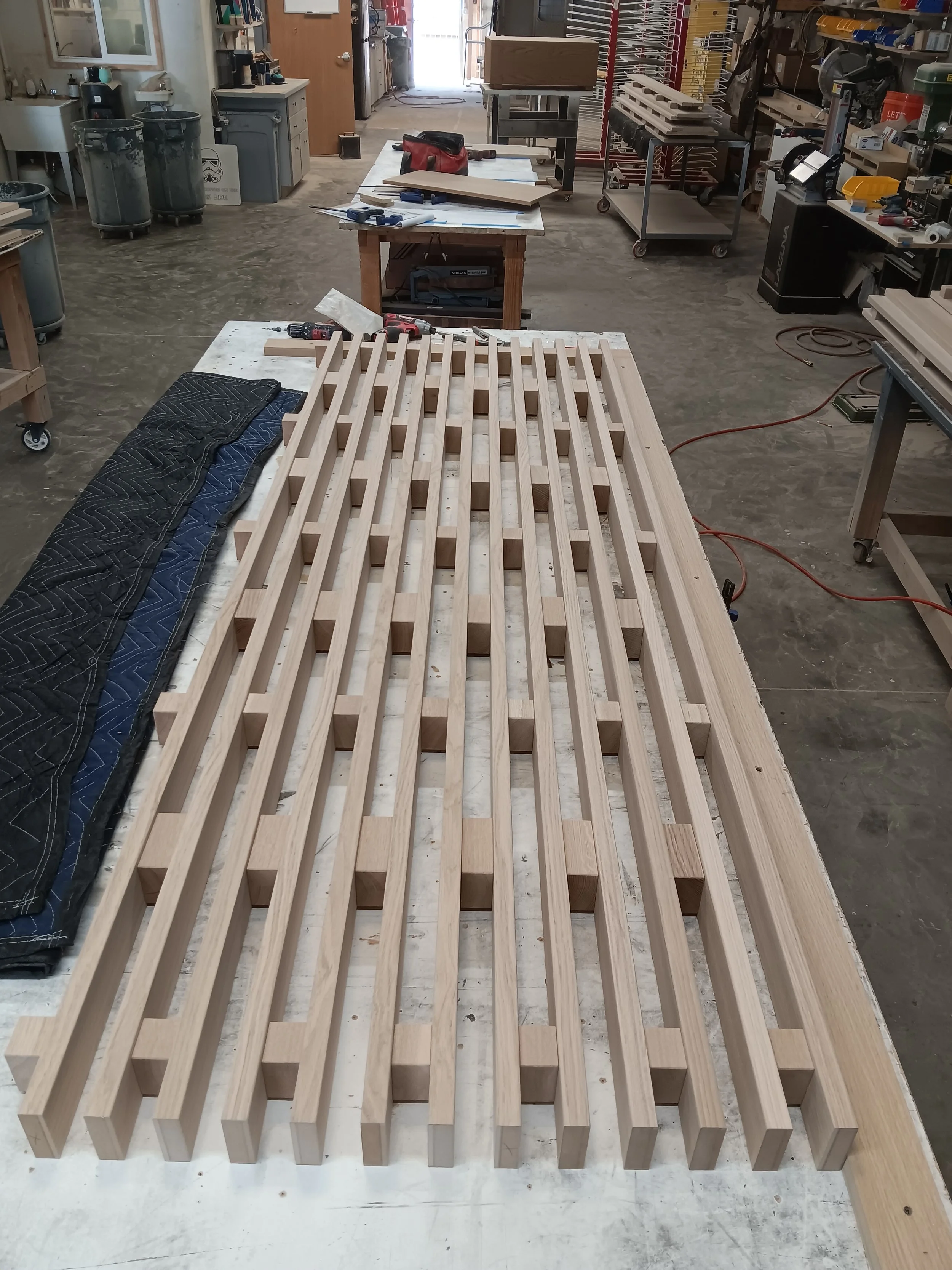 Wooden slats arranged in a grid pattern on a workshop table, surrounded by tools and workshop equipment.