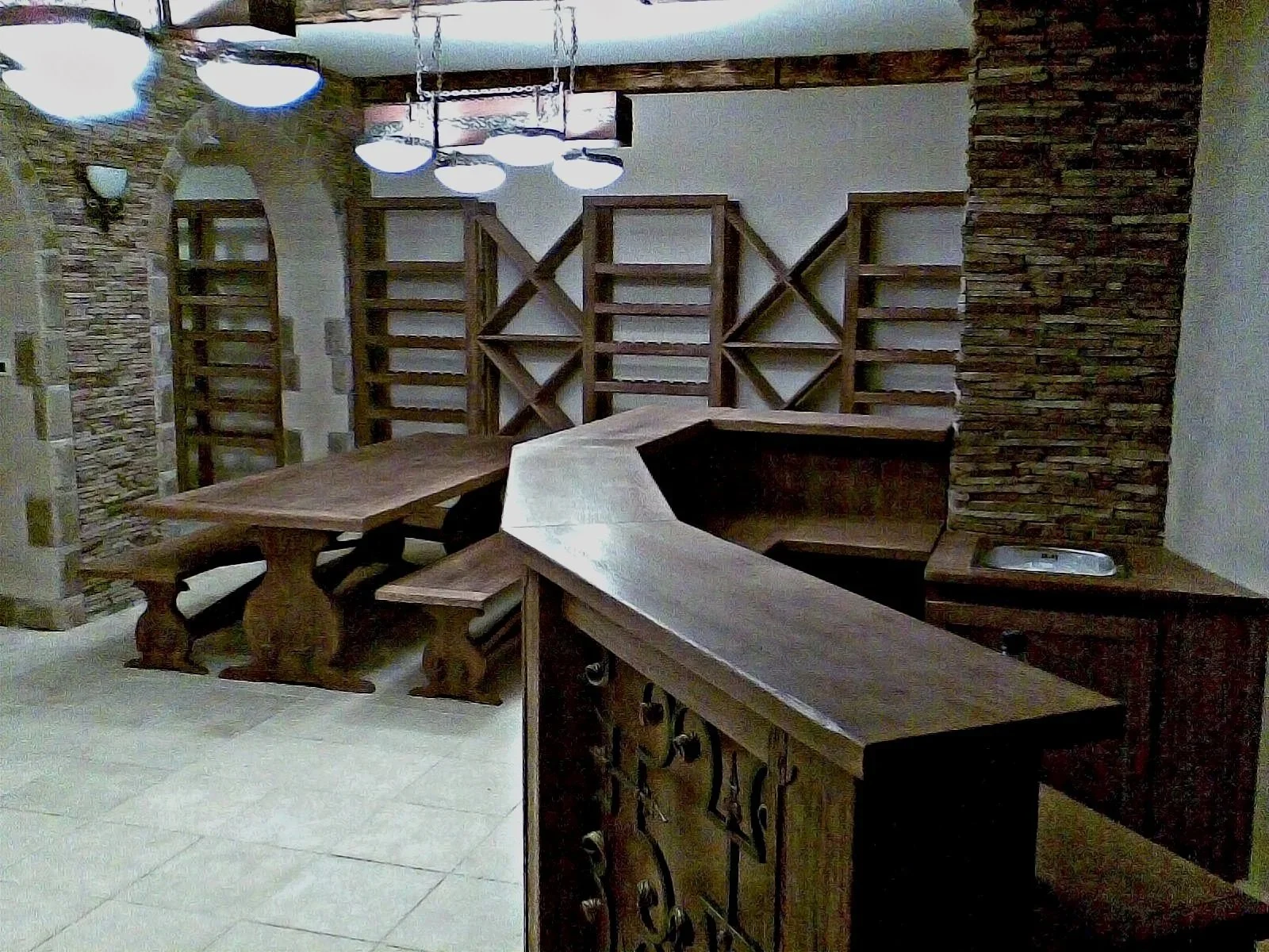 An interior space with unfinished wooden shelves and a large wooden table in a room with stone accent walls and tile flooring.