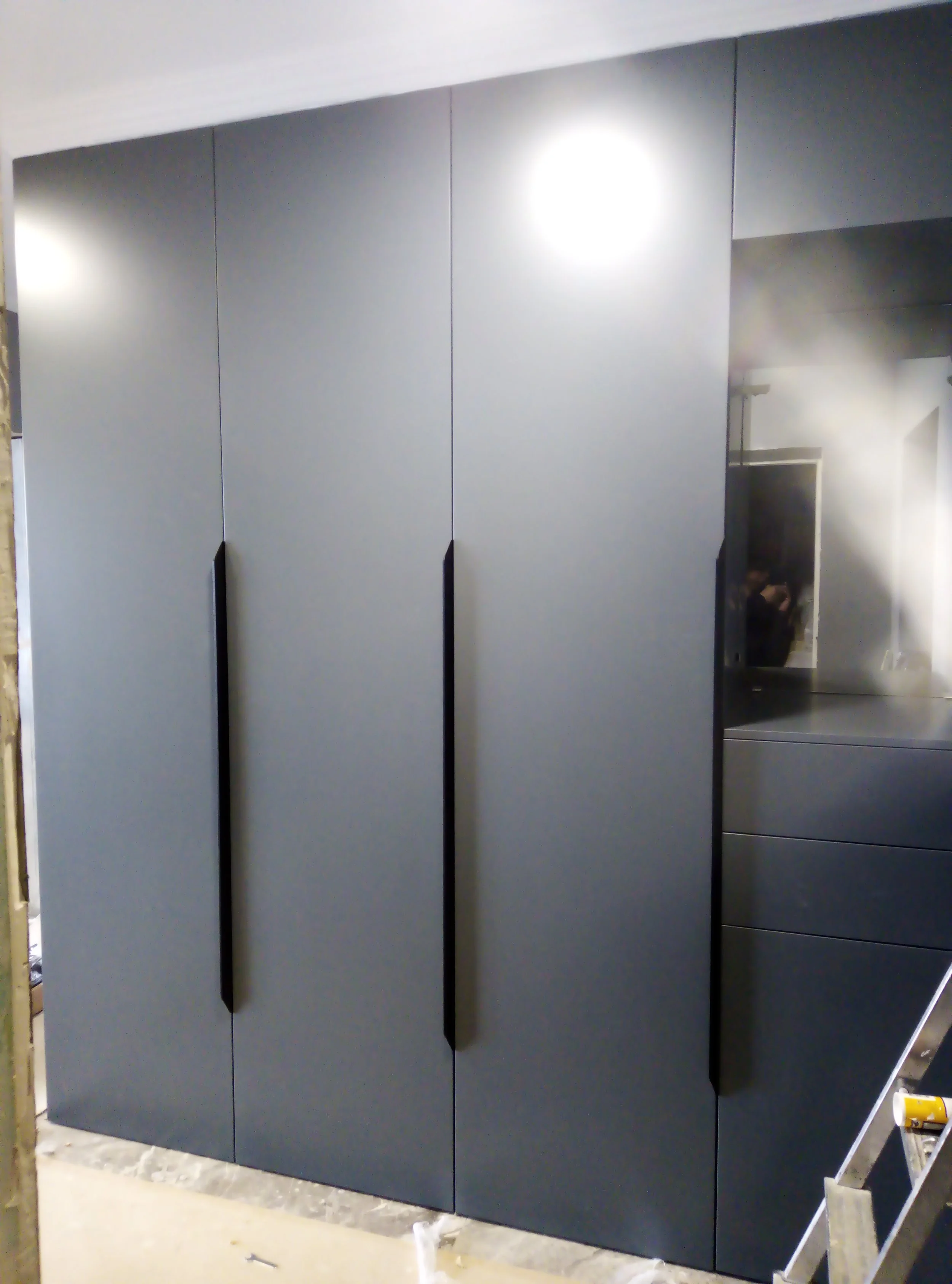 Modern gray cabinet with long black handles in a room under construction or renovation.
