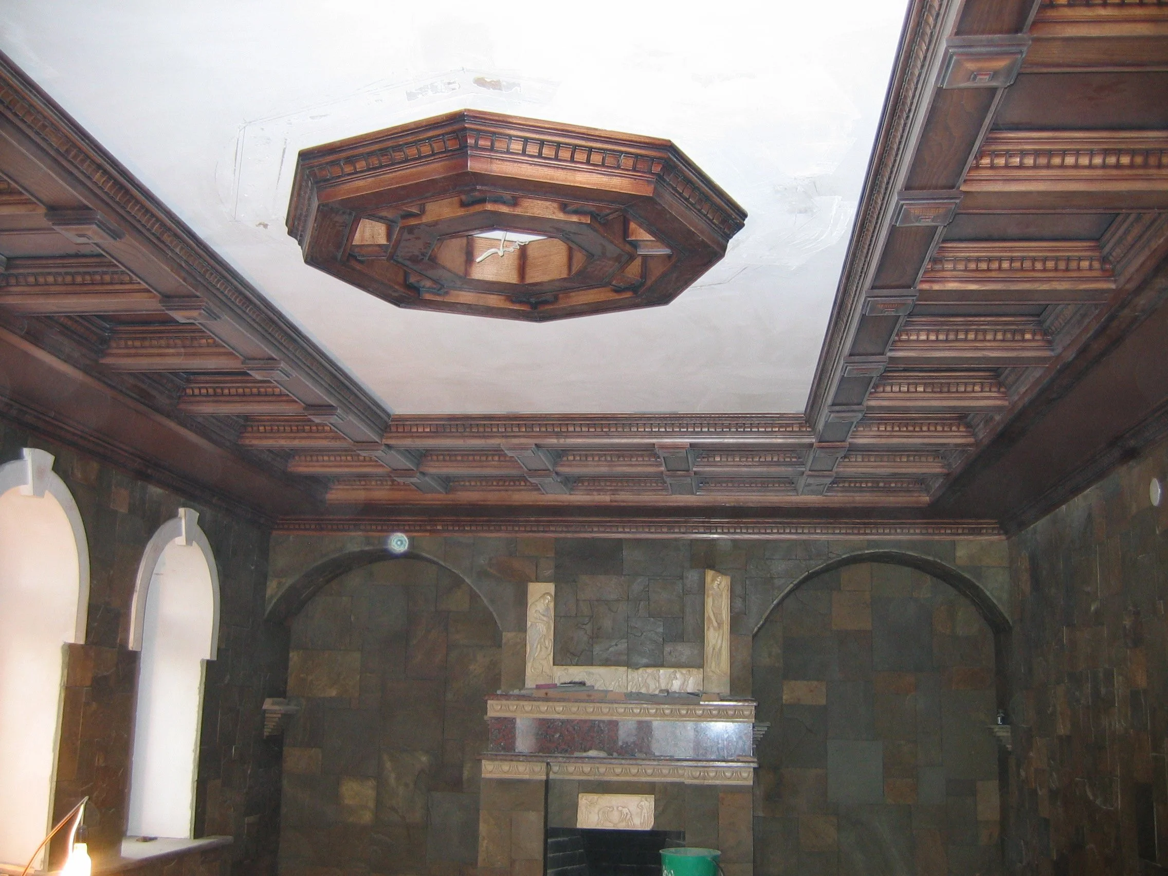 Interior of a room with dark wood paneling, a fireplace, and a ornate ceiling with a wooden medallion at the center.