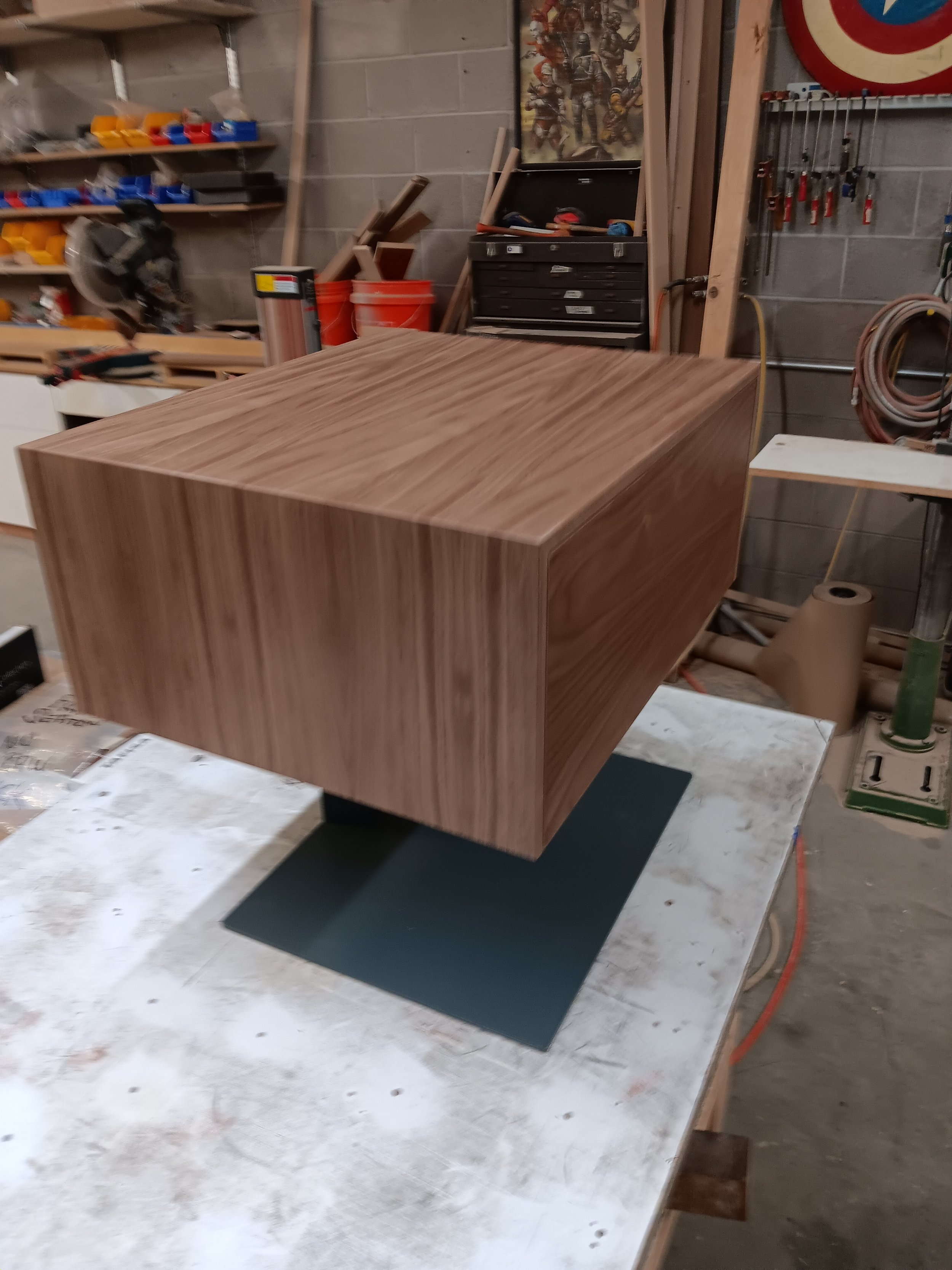 A wooden box or piece of furniture in a woodworking workshop, with tools and supplies visible in the background.