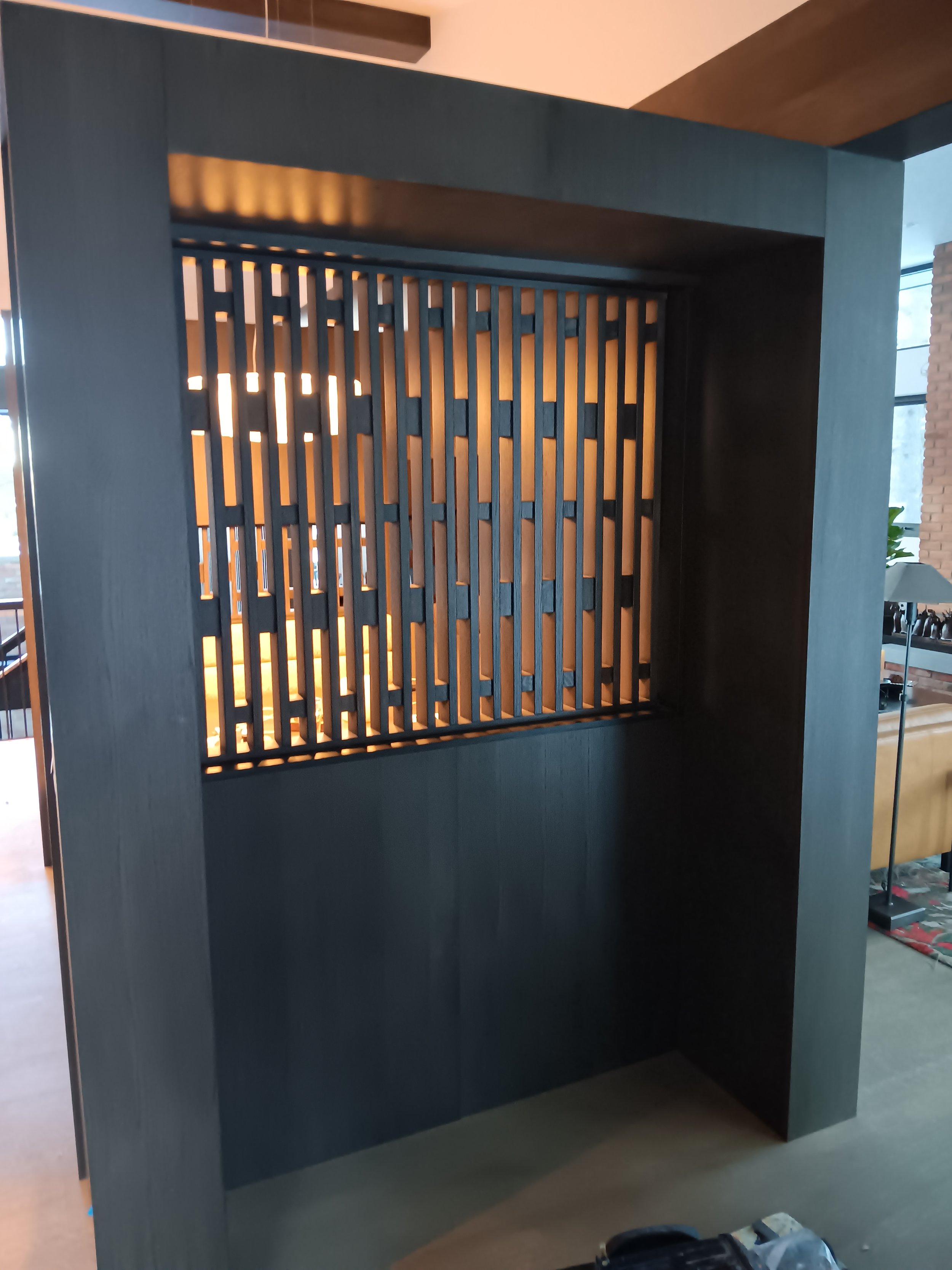 A modern, dark-colored wooden room divider with vertical slats and backlighting, situated in an interior space.