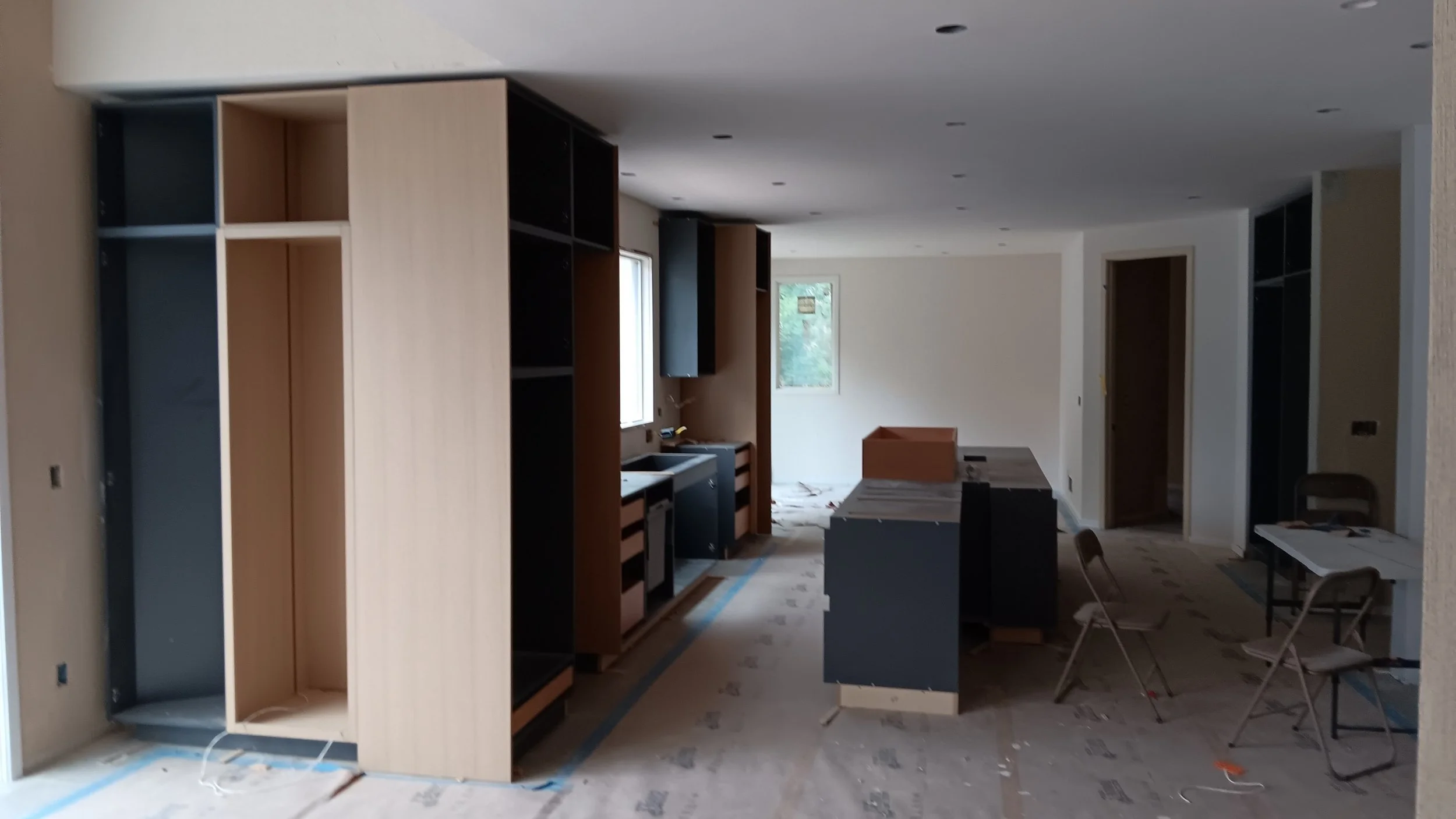 Interior of a room under construction with unfinished cabinets, a small table with chairs, and construction materials scattered on the floor.