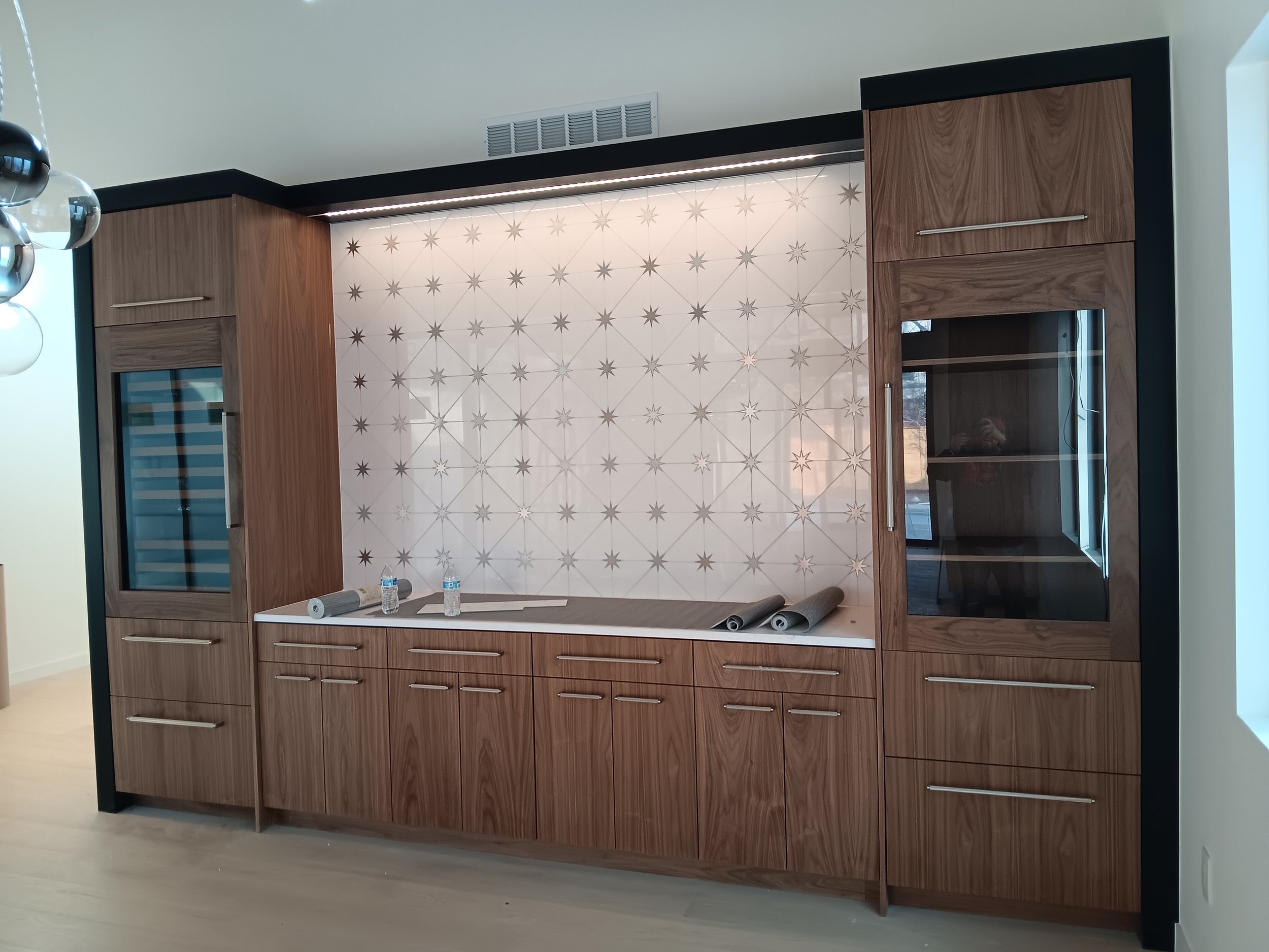 Modern kitchen cabinetry with wood finish, glass-fronted cabinets, and a decorative backsplash featuring a starburst pattern.