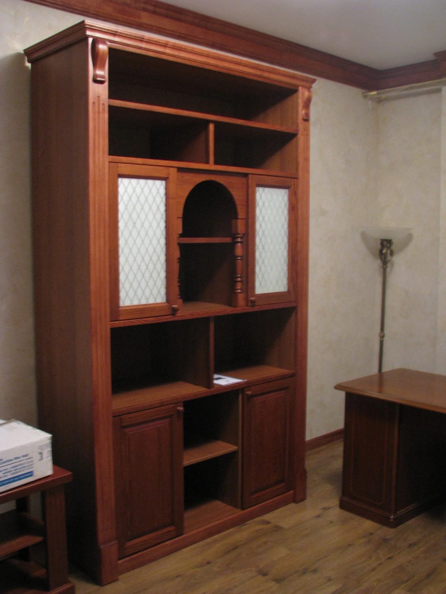 Wooden display cabinet with glass panes and open shelves in a room with beige walls and a wooden floor.