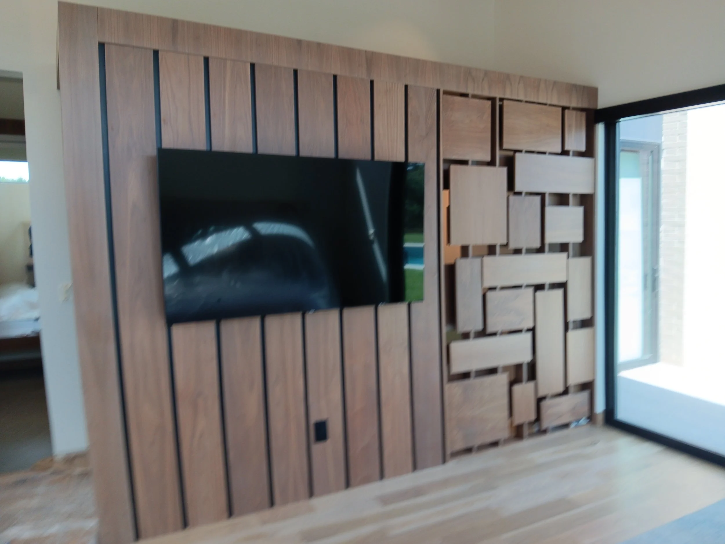 Living room with a wooden accent wall, mounted television, and a sliding glass door leading outside.