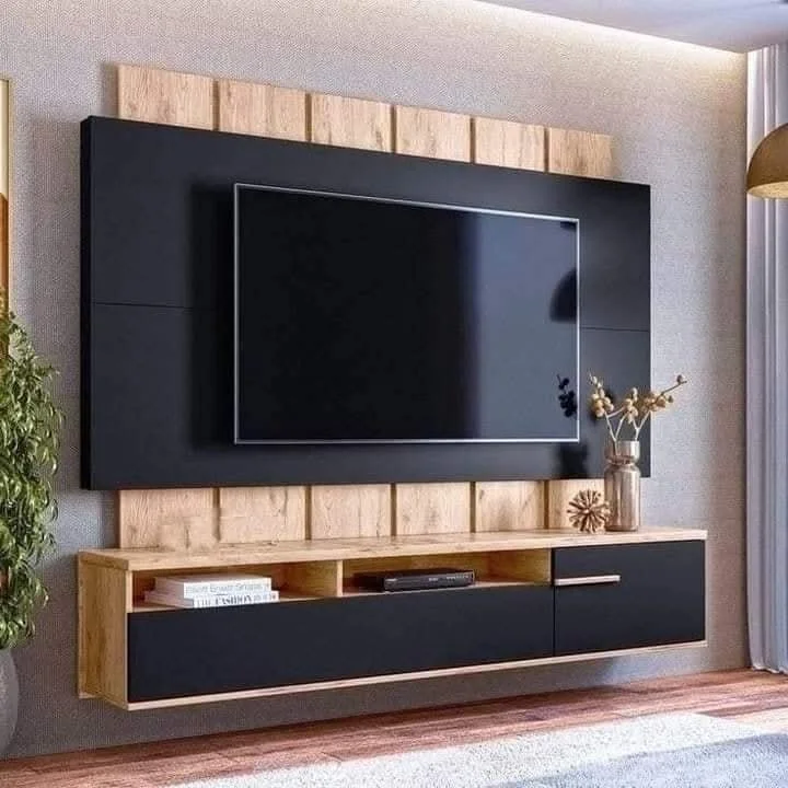 A modern living room entertainment wall with a mounted flat-screen TV, black and natural wood floating cabinet, and decorative items including a vase with dried flowers and a sculpture.