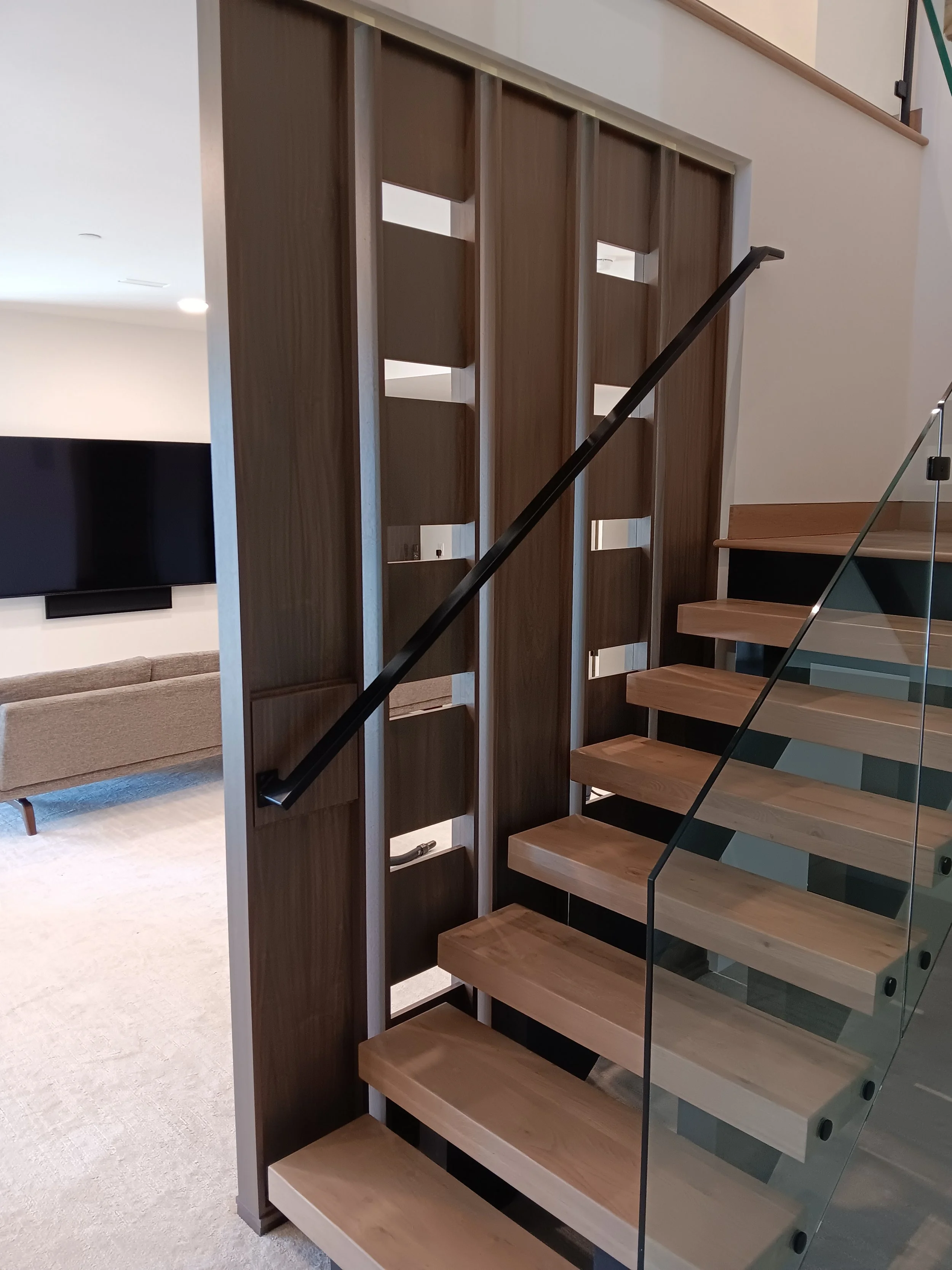 Wooden staircase with glass railing next to a decorative wooden partition with geometric cutouts.
