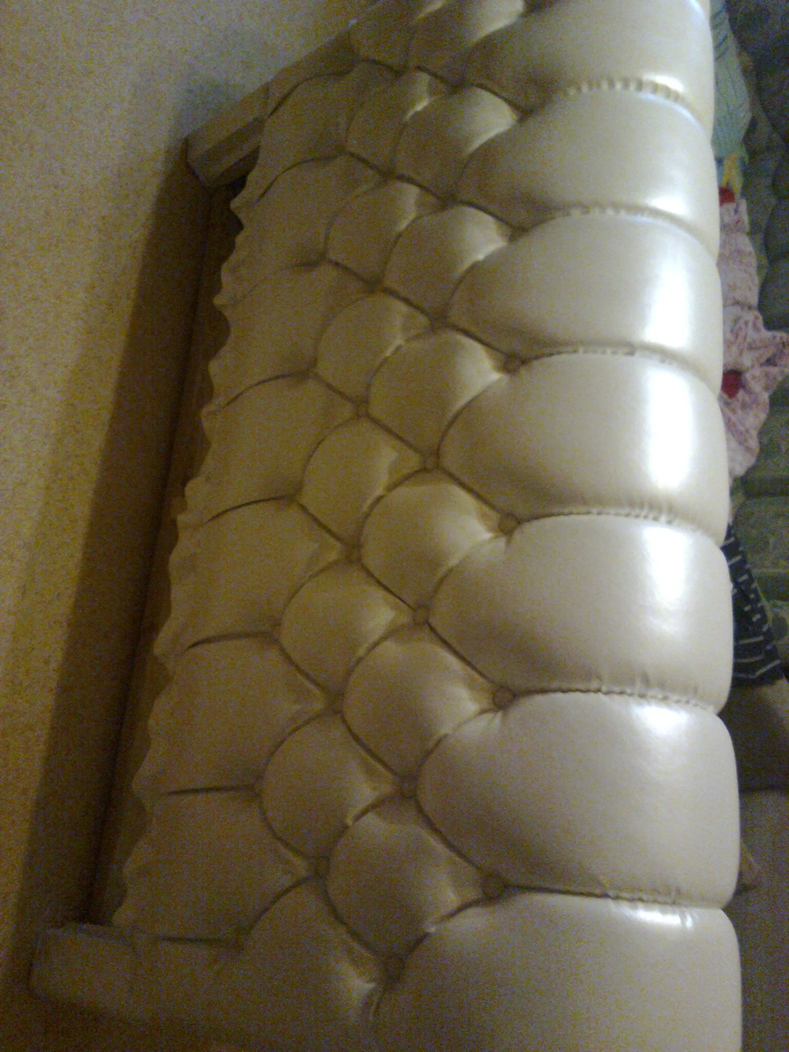 A beige tufted leather sofa with a textured pattern on beige carpeted flooring.