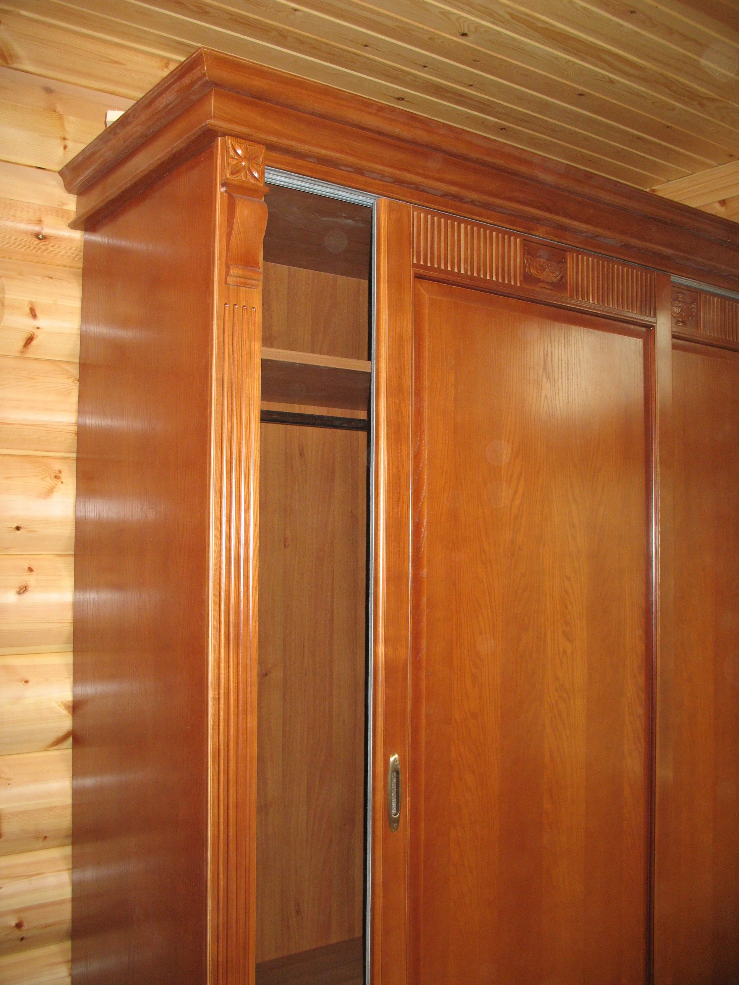 Wooden built-in closet with sliding door in a room with wood-paneled ceiling and wood wall.