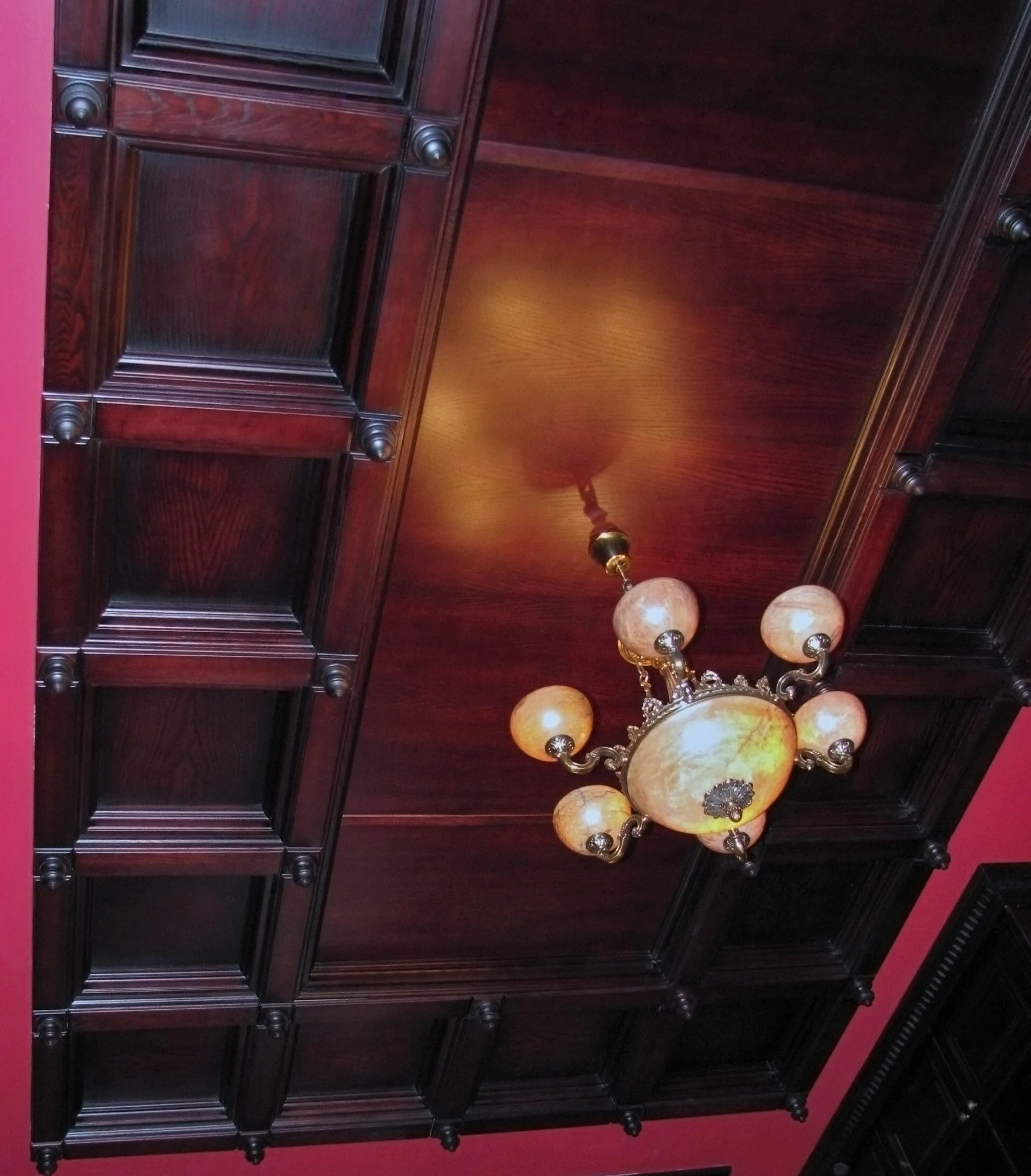Ceiling with dark wood paneling and a vintage chandelier with multiple glass globes.