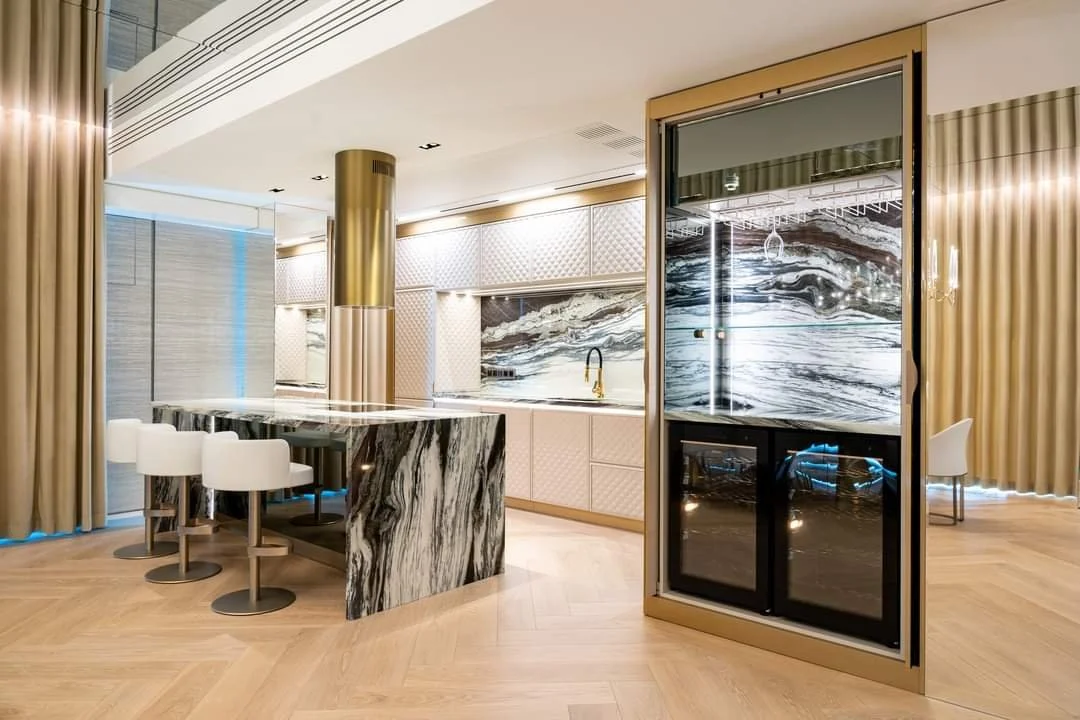 Modern kitchen with marble countertops and backsplash, beige cabinets, and a glass sliding door leading to a balcony with a marble-patterned outdoor wall.