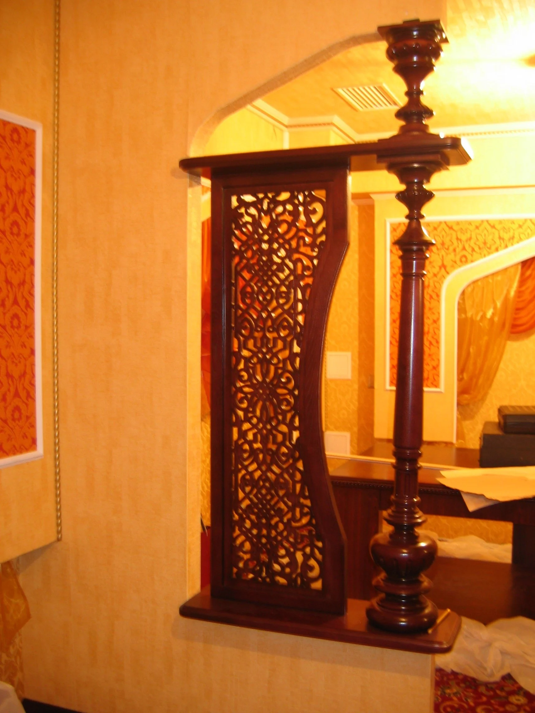 Close-up of a decorative wooden partition with intricate carved patterns, part of a traditional interior space with warm yellow and gold tones.