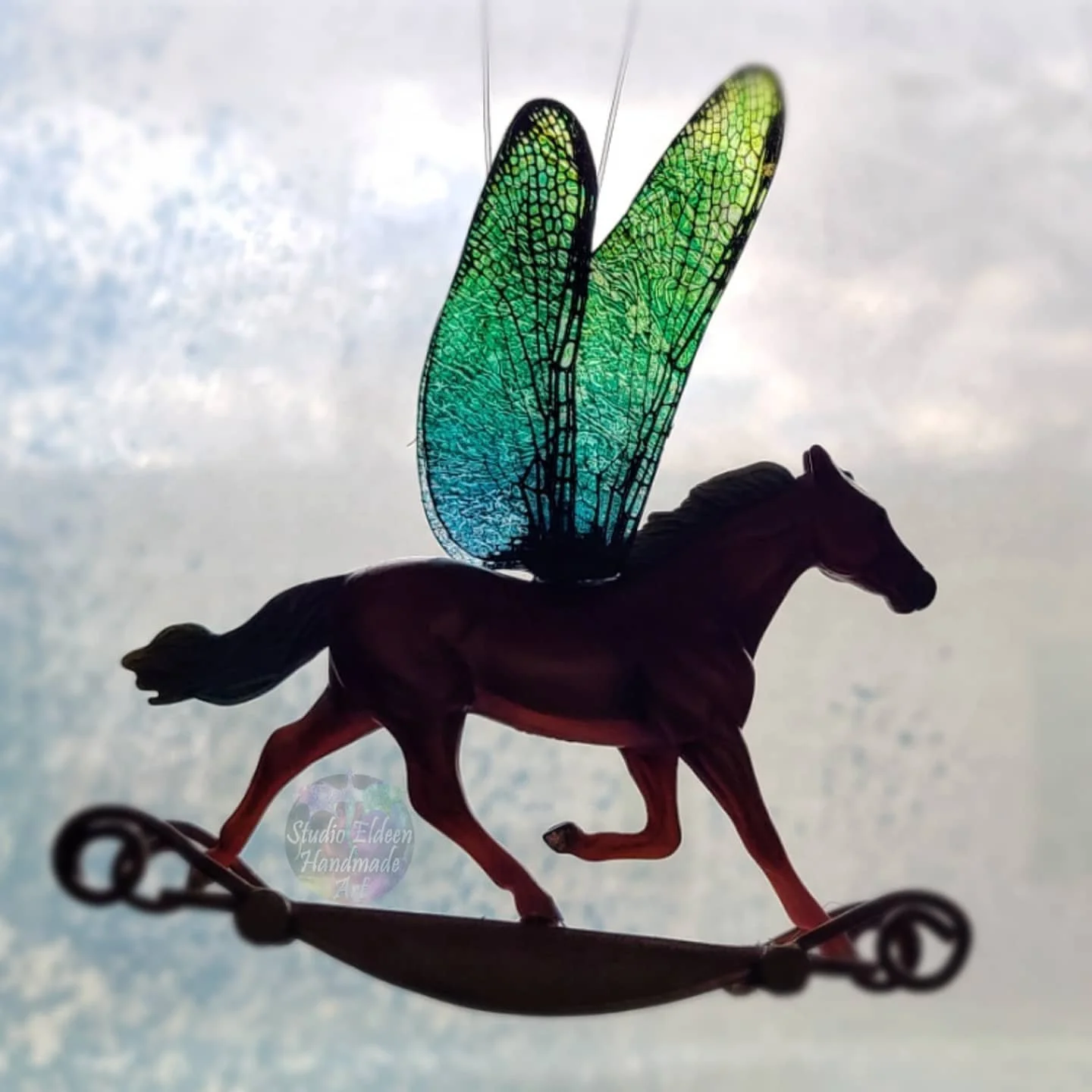 A silhouette of a decorative figurine of a rocking horse with dragonfly wings.