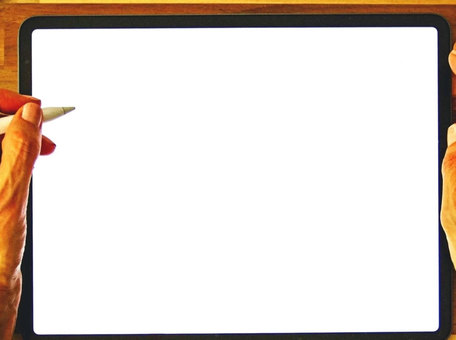 Hands holding a stylus over a tablet with a blank white screen on a wooden surface.