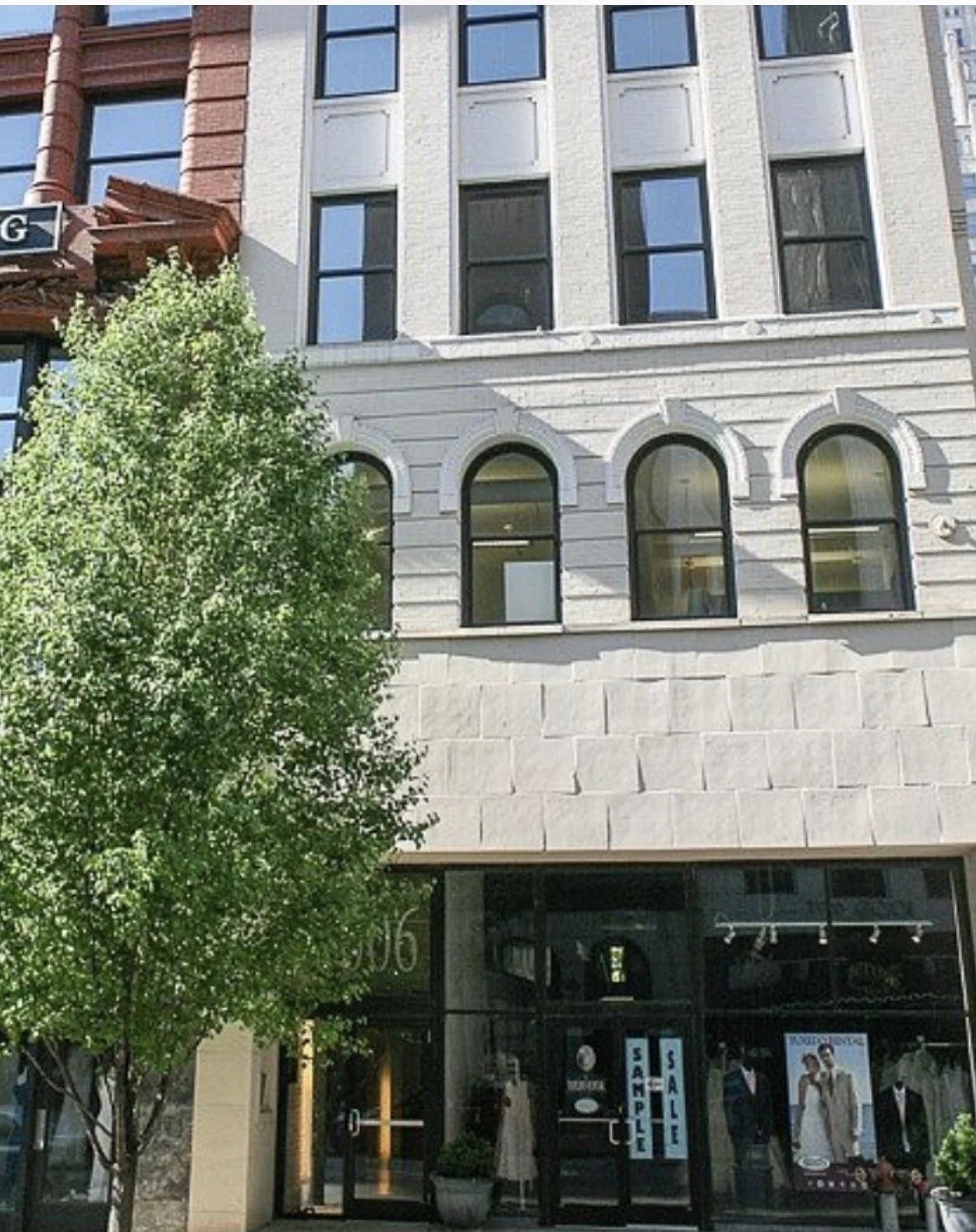 A multi-story building with large windows, a storefront with sale signs, mannequins displaying clothing, and a tree in front of the building.