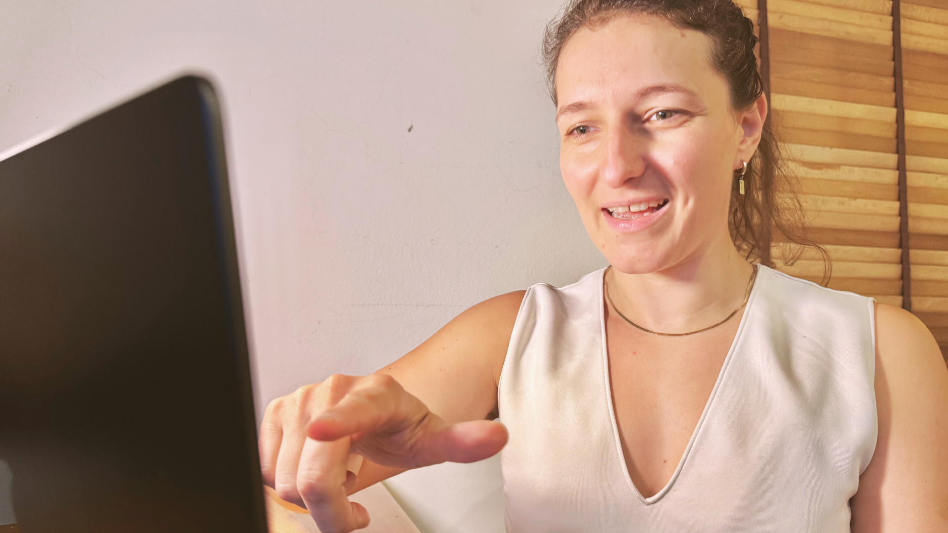A woman looking at a laptop screen smiling and pointing at it.