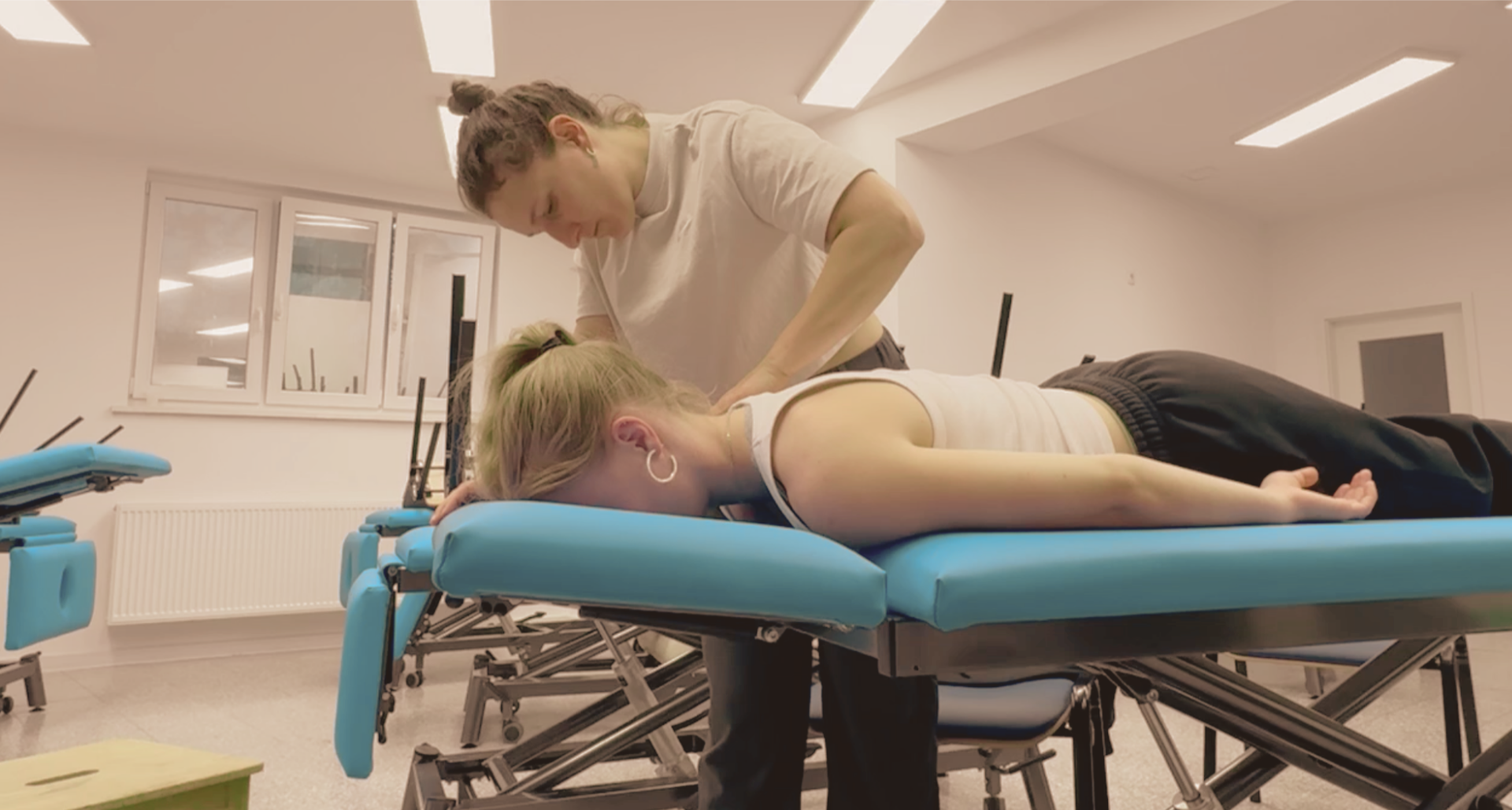 A massage therapist providing a massage to a woman lying face down on a massage table in a bright, clean room.