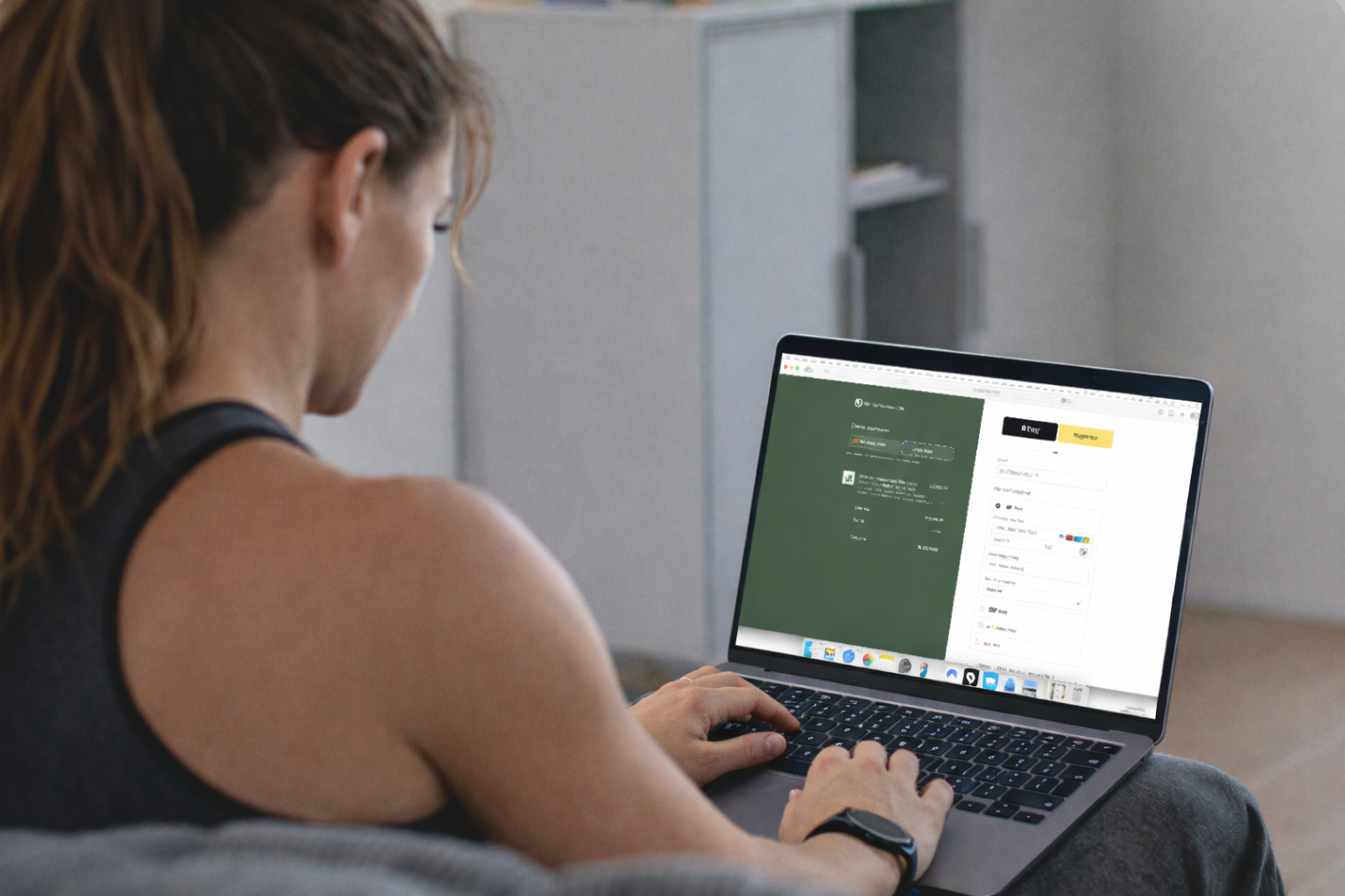 A woman with curly hair sitting on a gray couch using a laptop to sign up on a website, with the screen displaying a registration page.