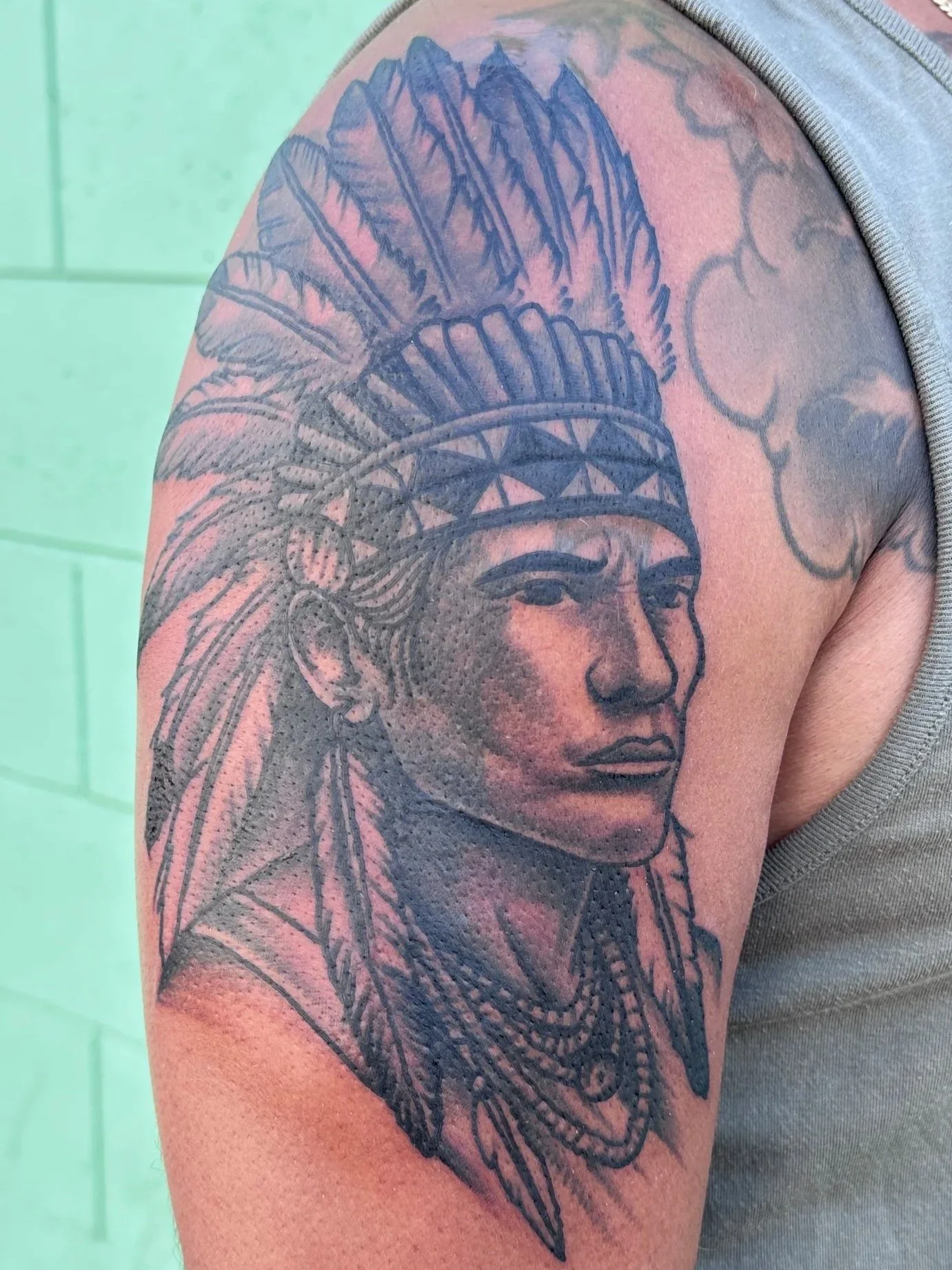 Tattoo of a Native American chief with a feathered headdress on a person's upper arm.