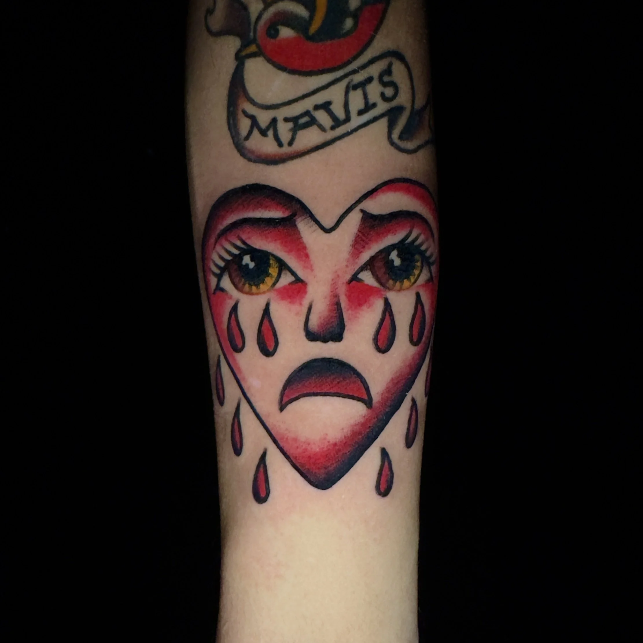 Tattoo of a crying heart-shaped face with large eyes, tears, and a sad expression, in a traditional tattoo style.