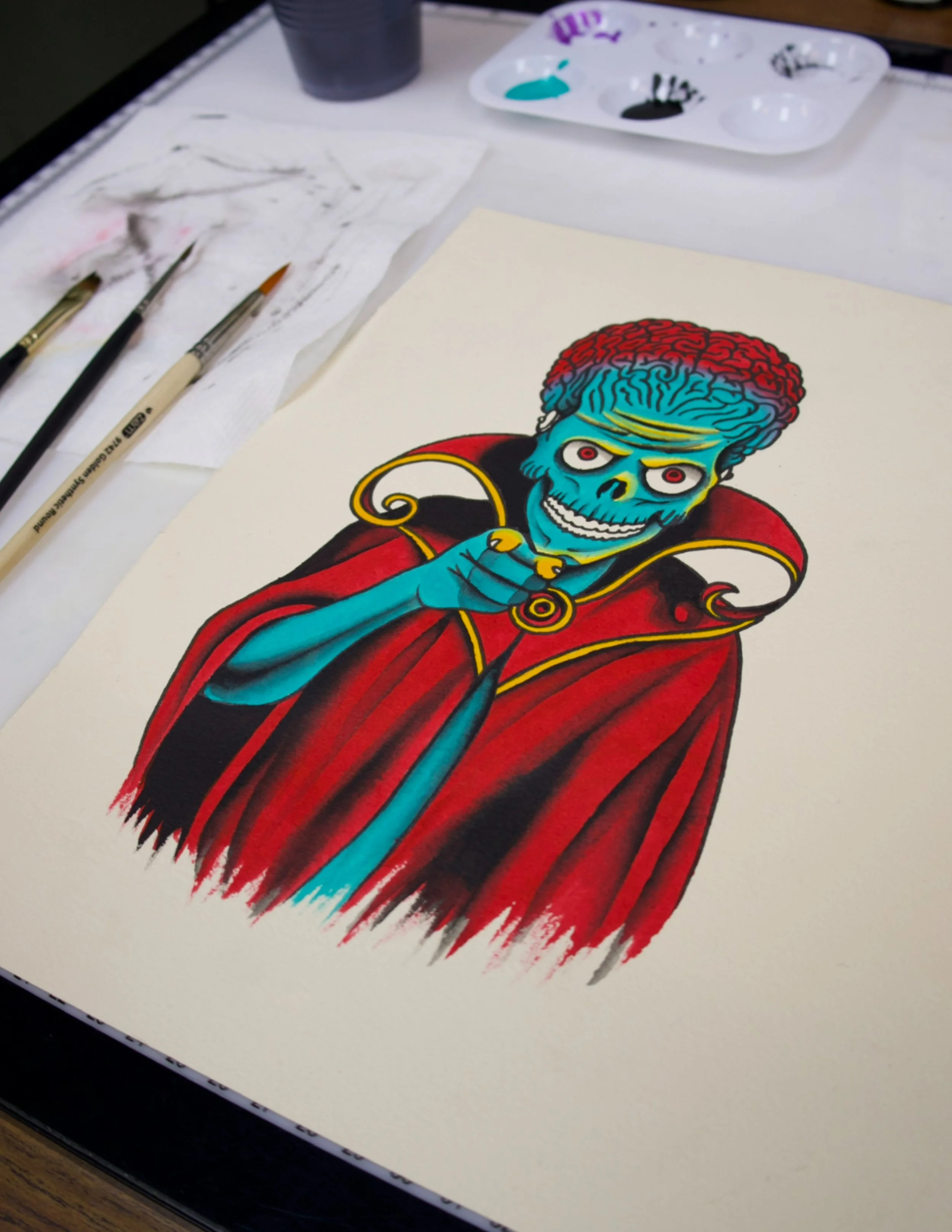 A colorful illustration of a skeleton with a brain-like head, wearing a red cape and a black and red outfit, pointing with one finger.