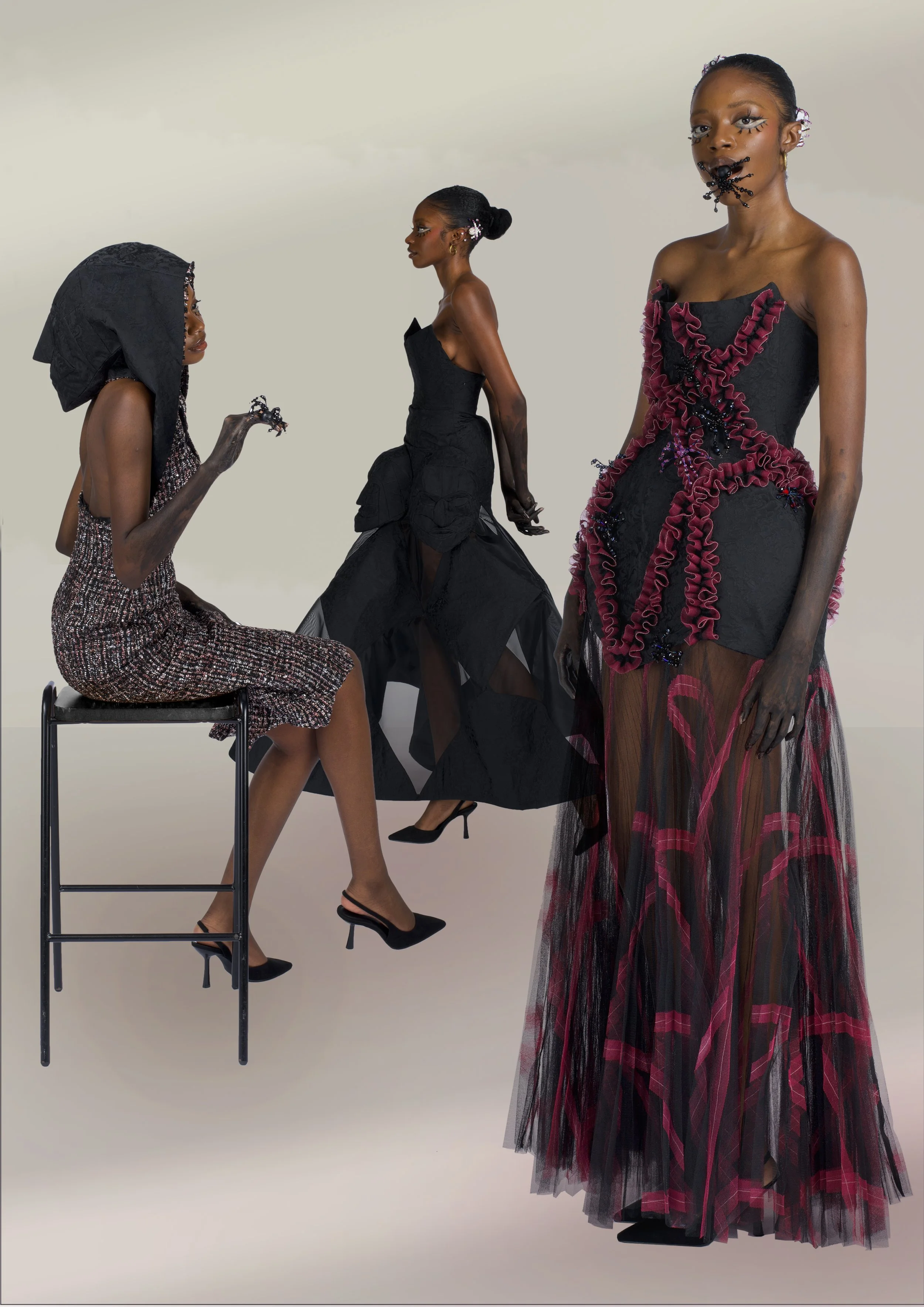 Three women wearing elaborate black and red fashion garments, with detailed accessories, posed on a light background.