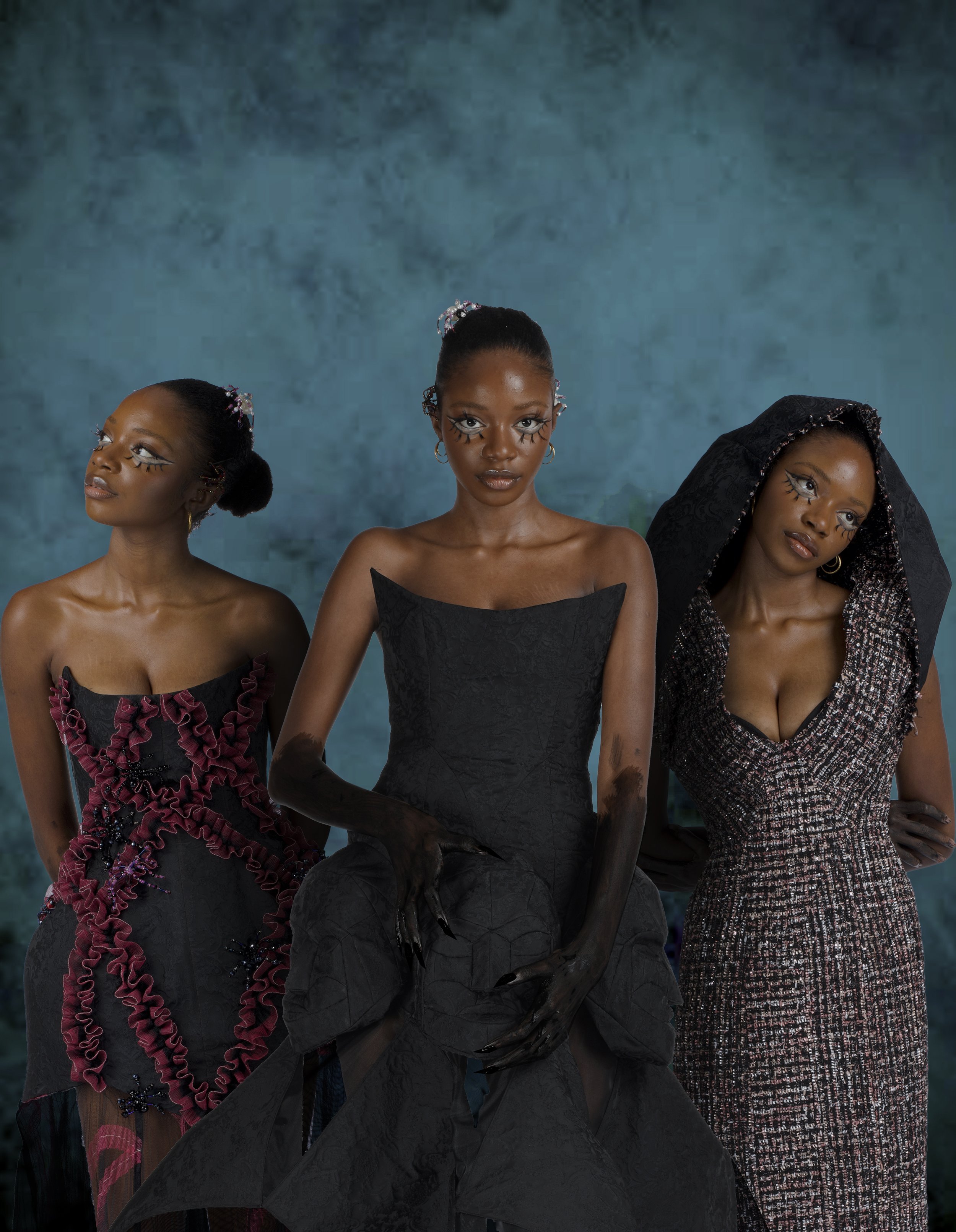 Three women with artistic makeup and styled hair, wearing elegant dresses, posing against a textured blue background.